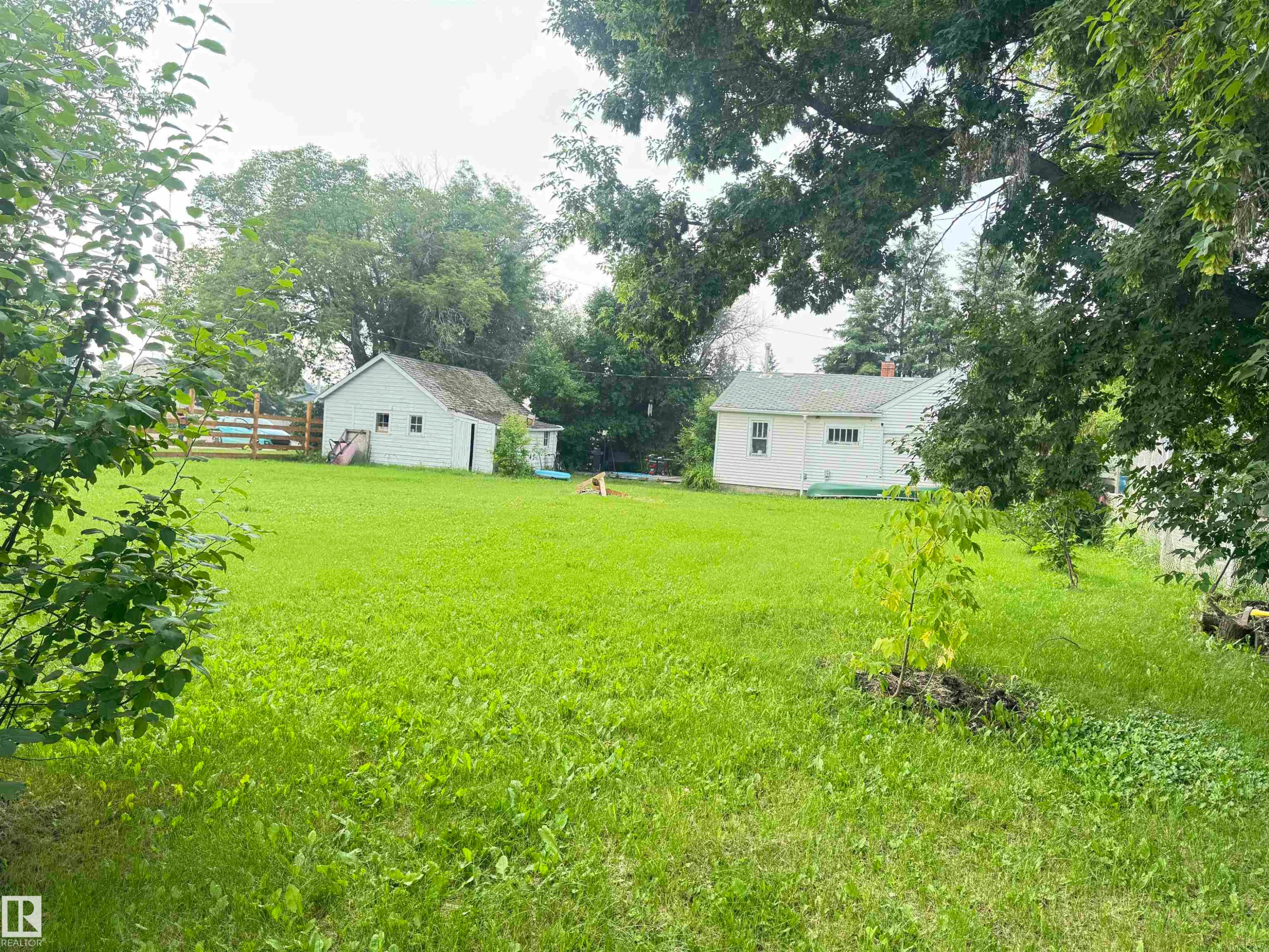 Expansive lawn with a detached shed and a white siding residence featuring a green roof - 5019 48 Avenue, Onoway, AB - Outdoor