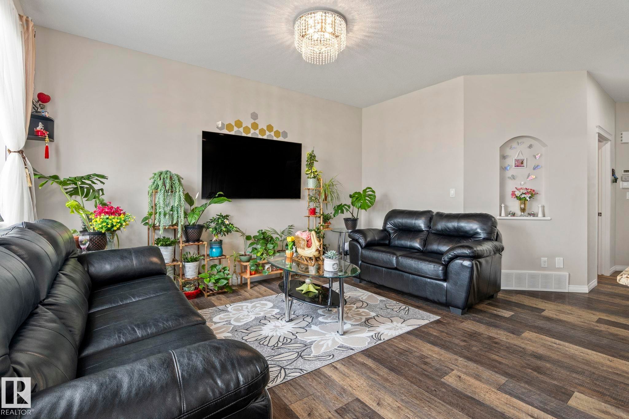 Living area featuring wood-finish flooring, a crystal chandelier, and an arched wall niche - 2131 51 Sw, Edmonton, AB - Indoor Photo Showing Living Room