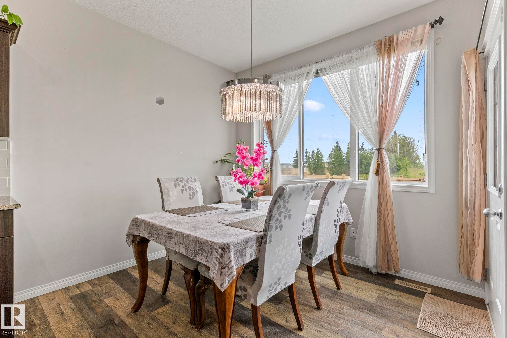 Spacious dining area featuring wood-finish flooring, a large window, and a contemporary chandelier - 2131 51 Sw, Edmonton, AB - Indoor Photo Showing Dining Room