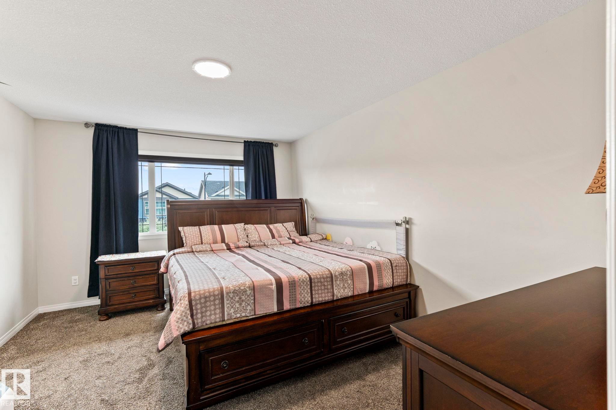 Carpeted bedroom with a large window, dark curtains, and a ceiling-mounted light fixture - 2131 51 Sw, Edmonton, AB - Indoor Photo Showing Bedroom