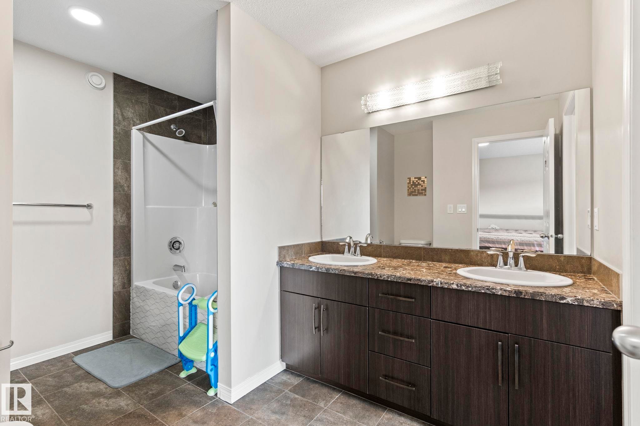 Bathroom featuring a dual-sink vanity with a speckled countertop, dark wood-finish cabinetry, and a full-width mirror - 2131 51 Sw, Edmonton, AB - Indoor Photo Showing Bathroom