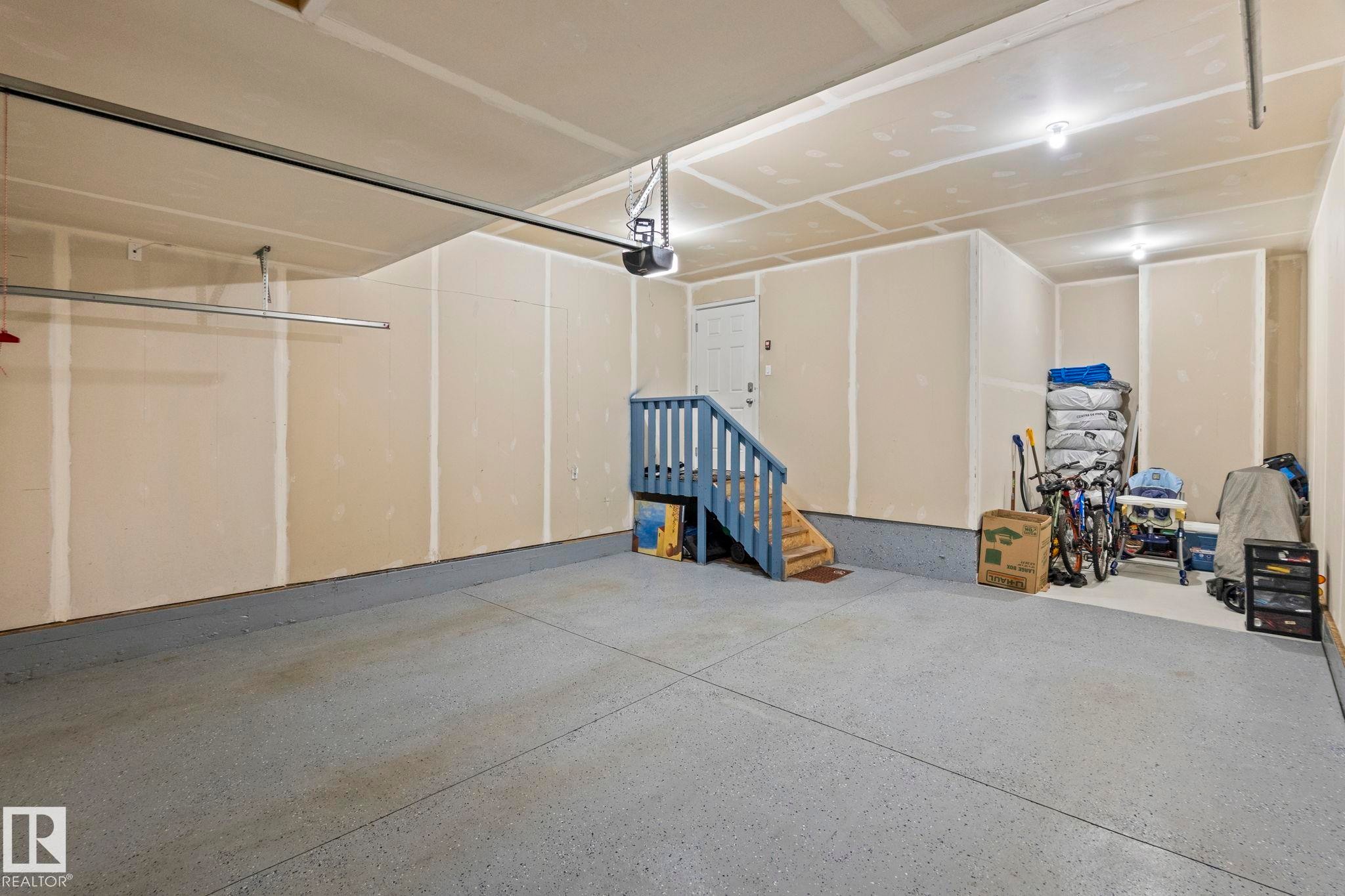 Spacious garage featuring a durable epoxy floor coating, interior access door, and a built-in staircase - 2131 51 Sw, Edmonton, AB - Indoor Photo Showing Garage