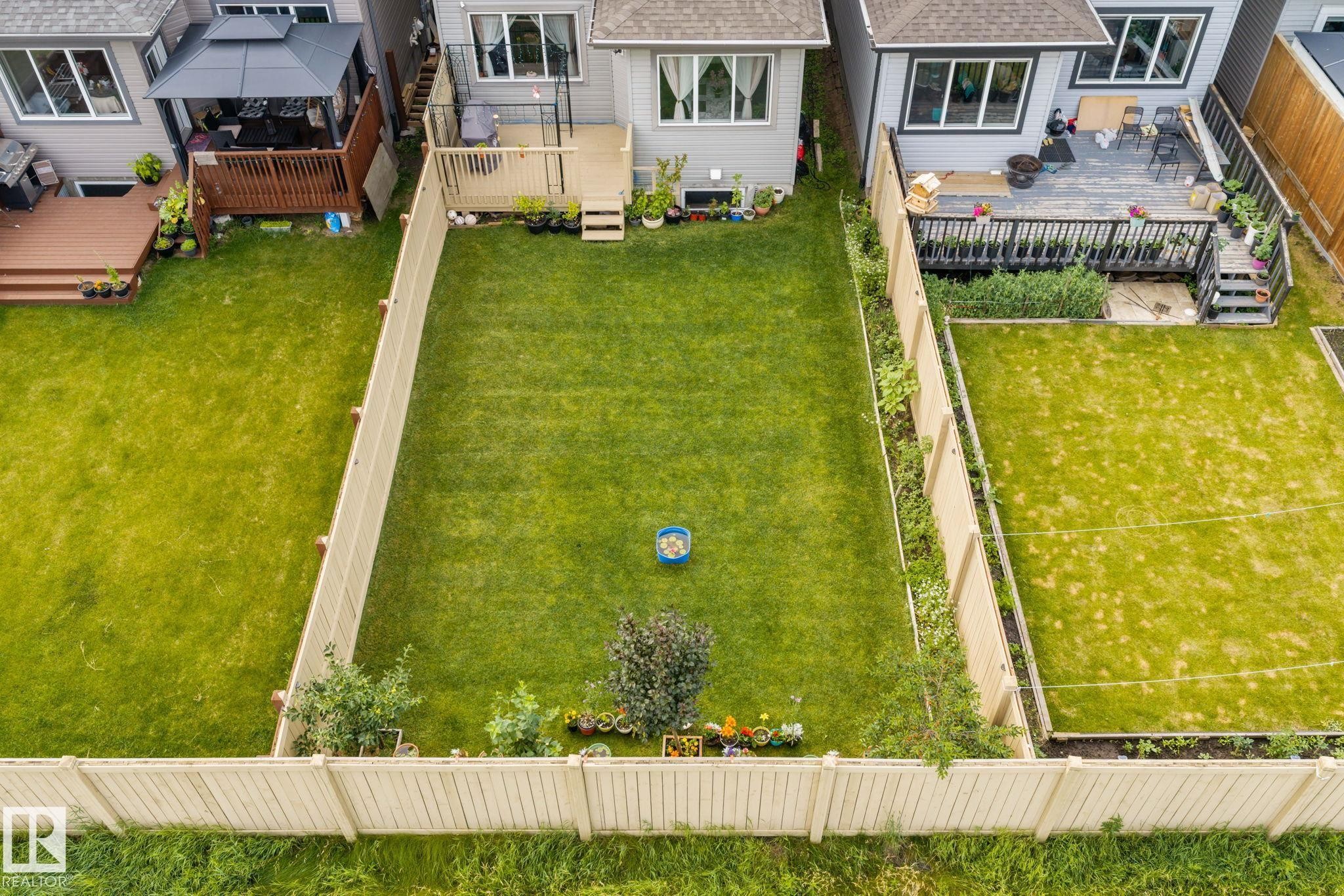 Expansive, fenced backyard featuring a large green lawn, mature plantings, and a private deck - 2131 51 Sw, Edmonton, AB - Outdoor