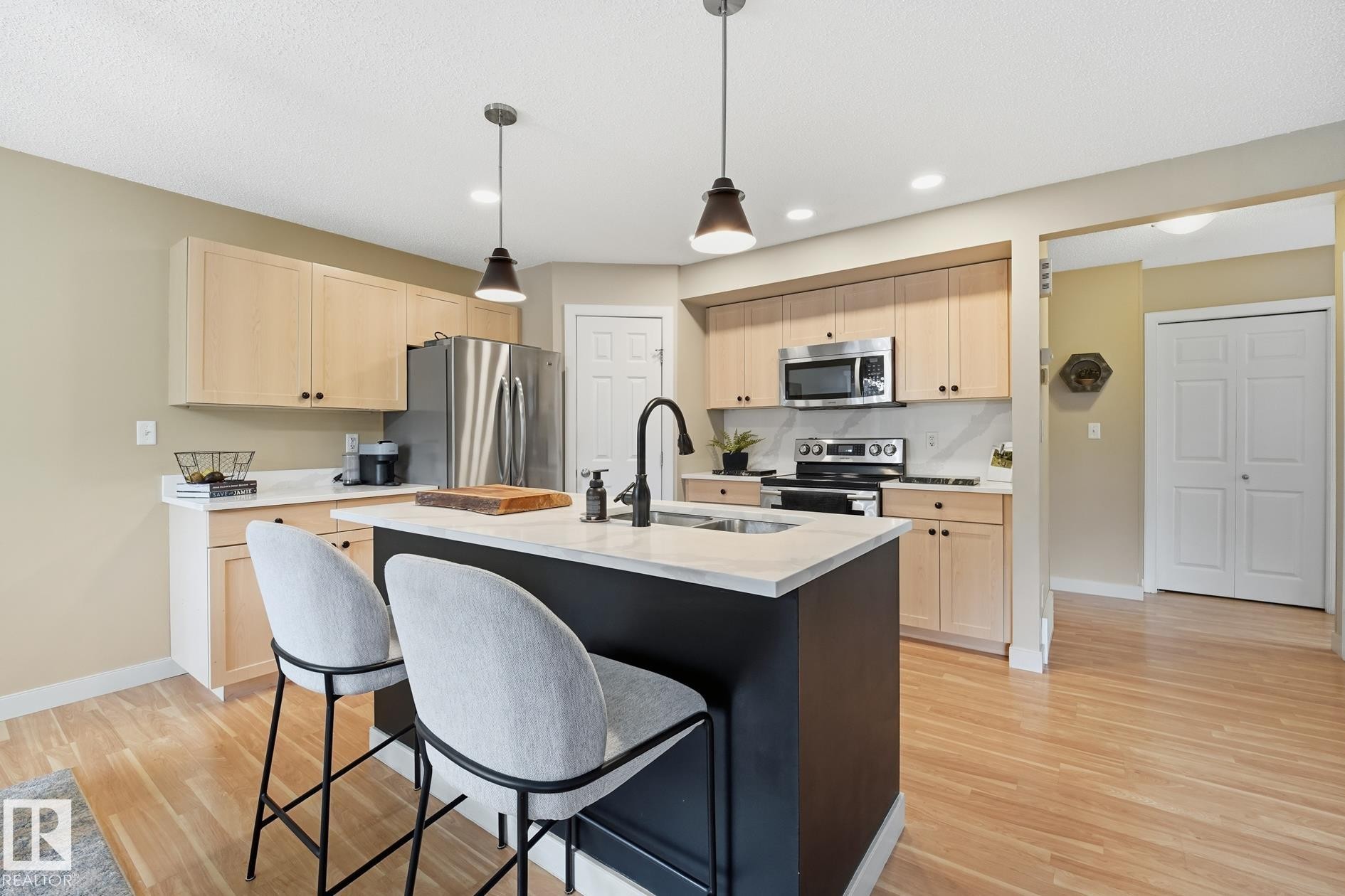 Kitchen featuring a central island with an undermount sink, pendant lighting, stainless steel appliances, and light wood-finish flooring - 20007 131 Avenue Nw, Edmonton, AB