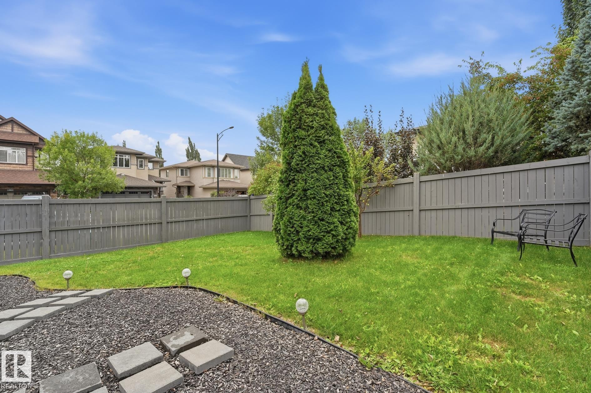 Expansive backyard featuring a manicured lawn, full-height privacy fencing, and a decorative stone pathway - 20007 131 Avenue Nw, Edmonton, AB