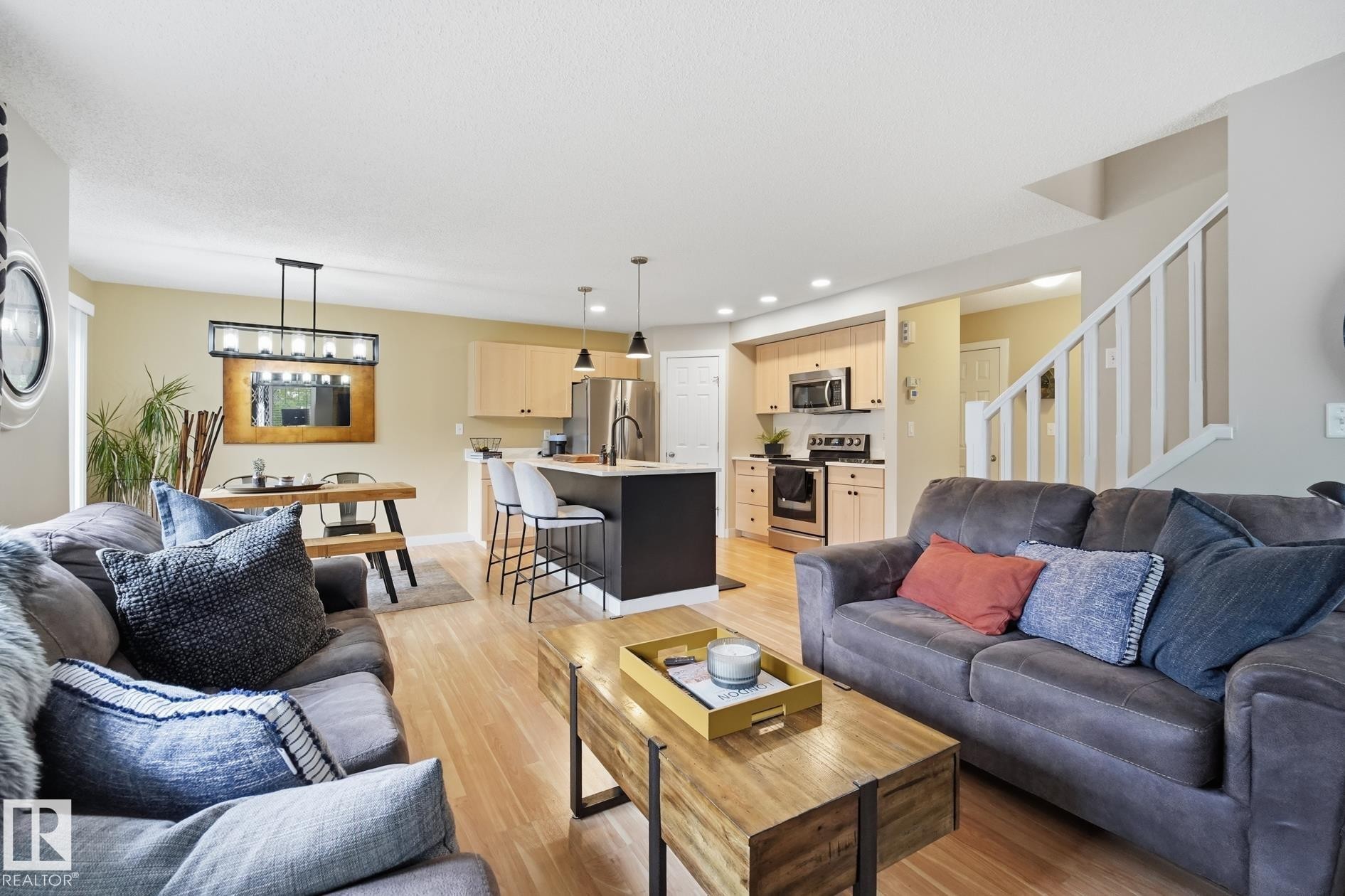 Open-concept living space featuring wood-finish flooring, a kitchen island with pendant lighting, stainless steel appliances, and light-toned cabinetry - 20007 131 Avenue Nw, Edmonton, AB