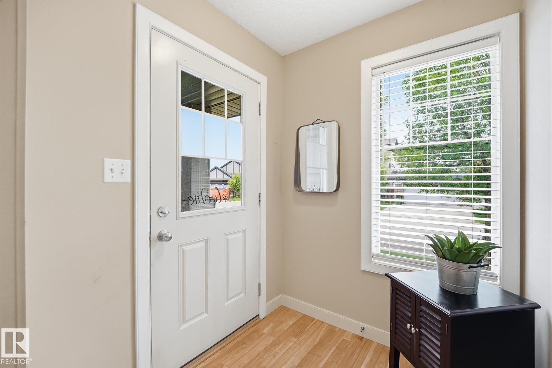 Entryway featuring a white paneled door with glass inserts, wood-finish flooring, a window with horizontal blinds, and neutral wall tones - 20007 131 Avenue Nw, Edmonton, AB