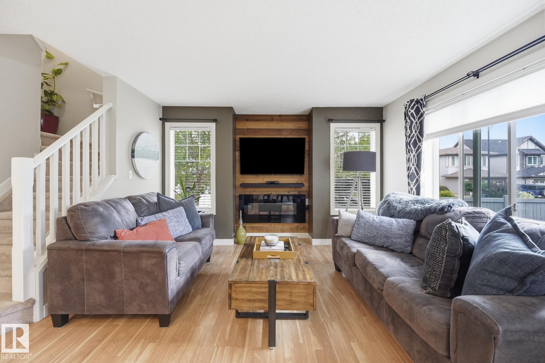 Light wood-finish flooring, staircase with white railings, integrated wall-mounted fireplace, and large windows - 20007 131 Avenue Nw, Edmonton, AB