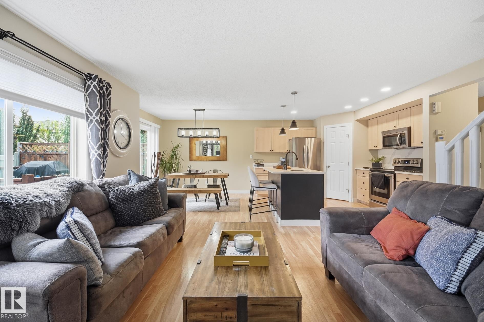 Open-concept living space featuring wood-finish flooring, a kitchen island with pendant lighting, stainless steel appliances, and light wood cabinetry - 20007 131 Avenue Nw, Edmonton, AB