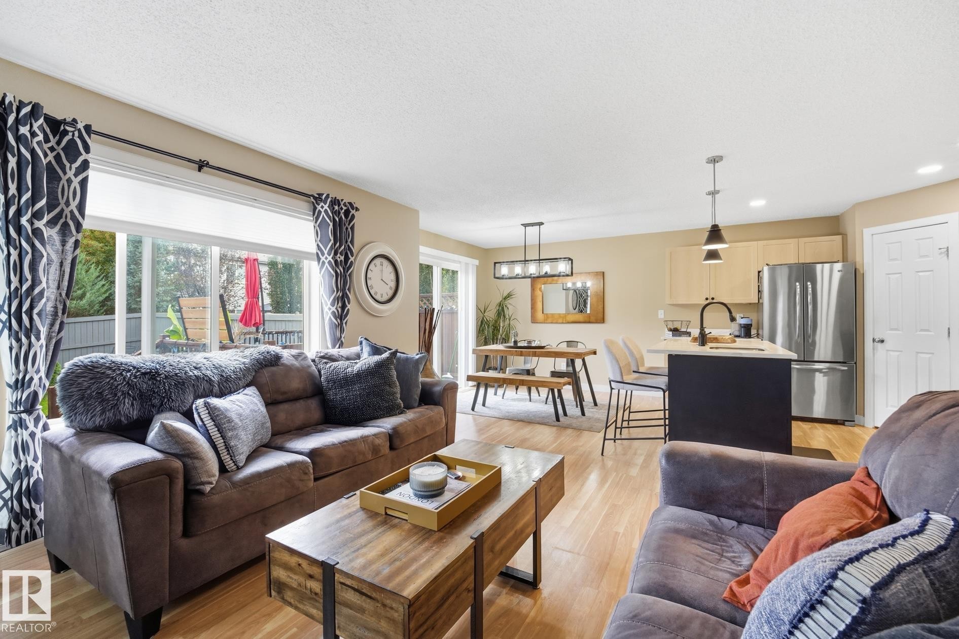 Open-concept living area featuring wood-finish flooring, sliding glass doors, a kitchen island with pendant lighting, and stainless steel appliances - 20007 131 Avenue Nw, Edmonton, AB