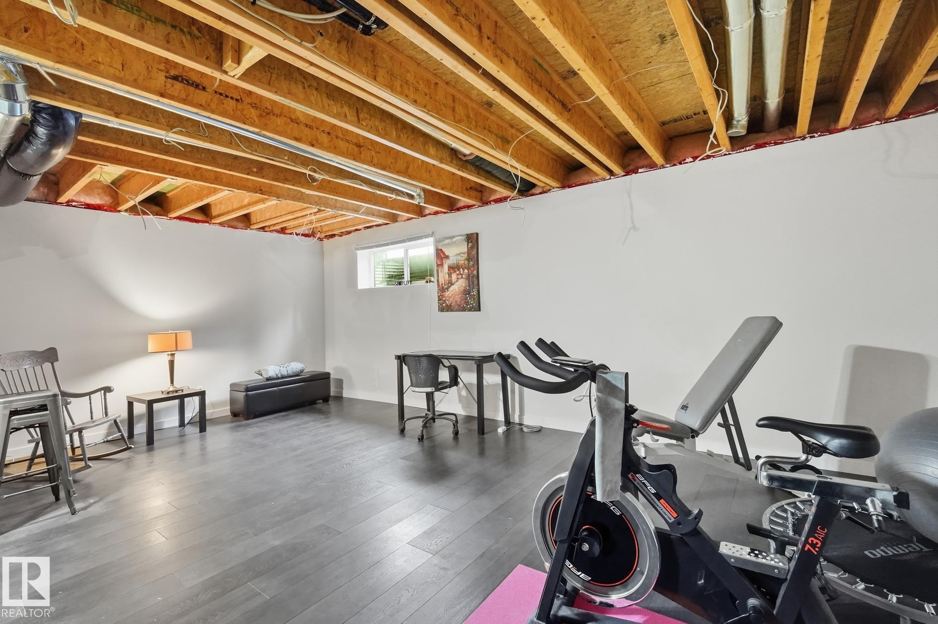 Basement space featuring exposed ceiling joists, white painted walls, wood-finish flooring, and a single window - 20007 131 Avenue Nw, Edmonton, AB