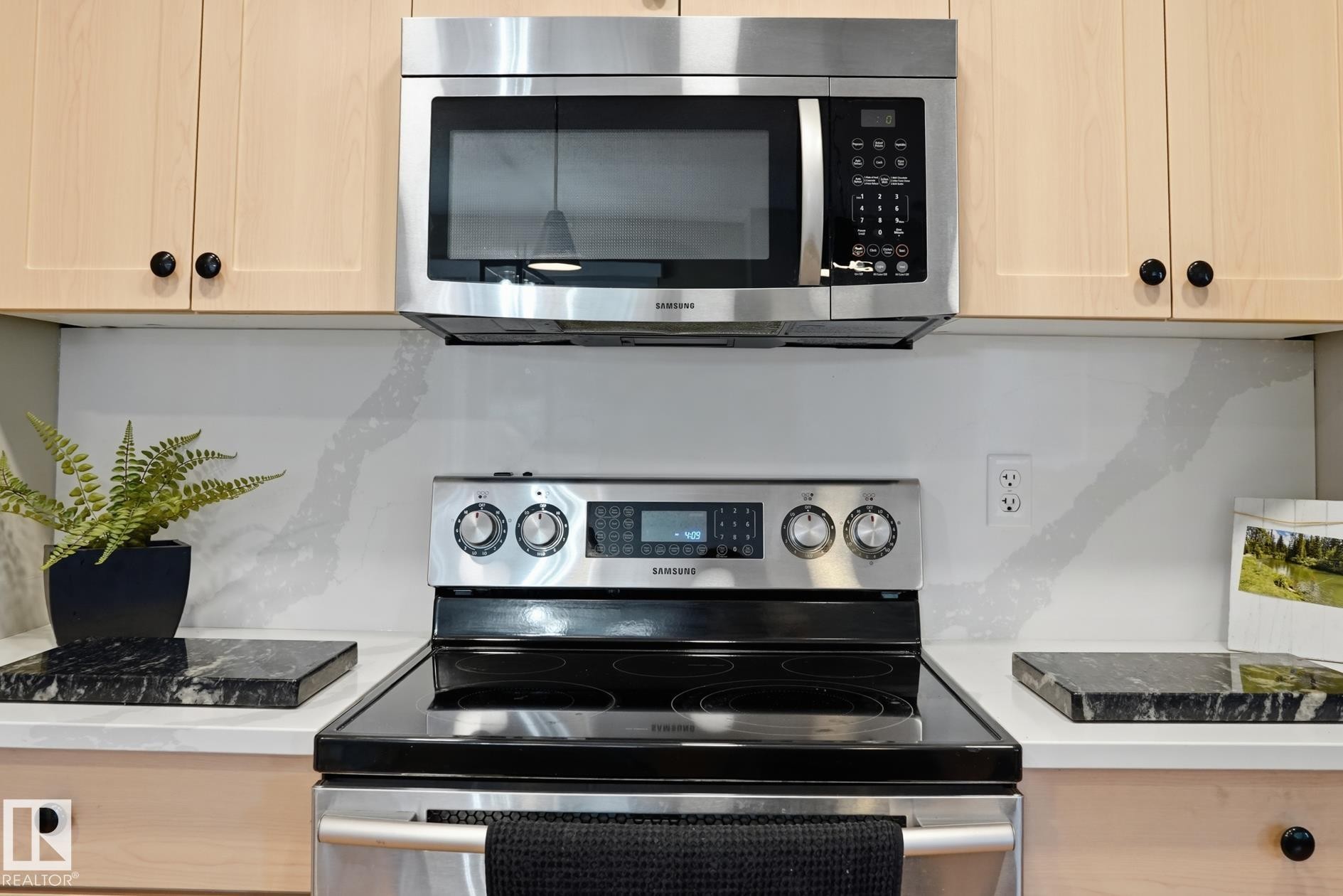 Stainless steel microwave, electric range with a smooth cooktop, light-toned cabinetry with black hardware, and a white countertop with a veined backsplash - 20007 131 Avenue Nw, Edmonton, AB