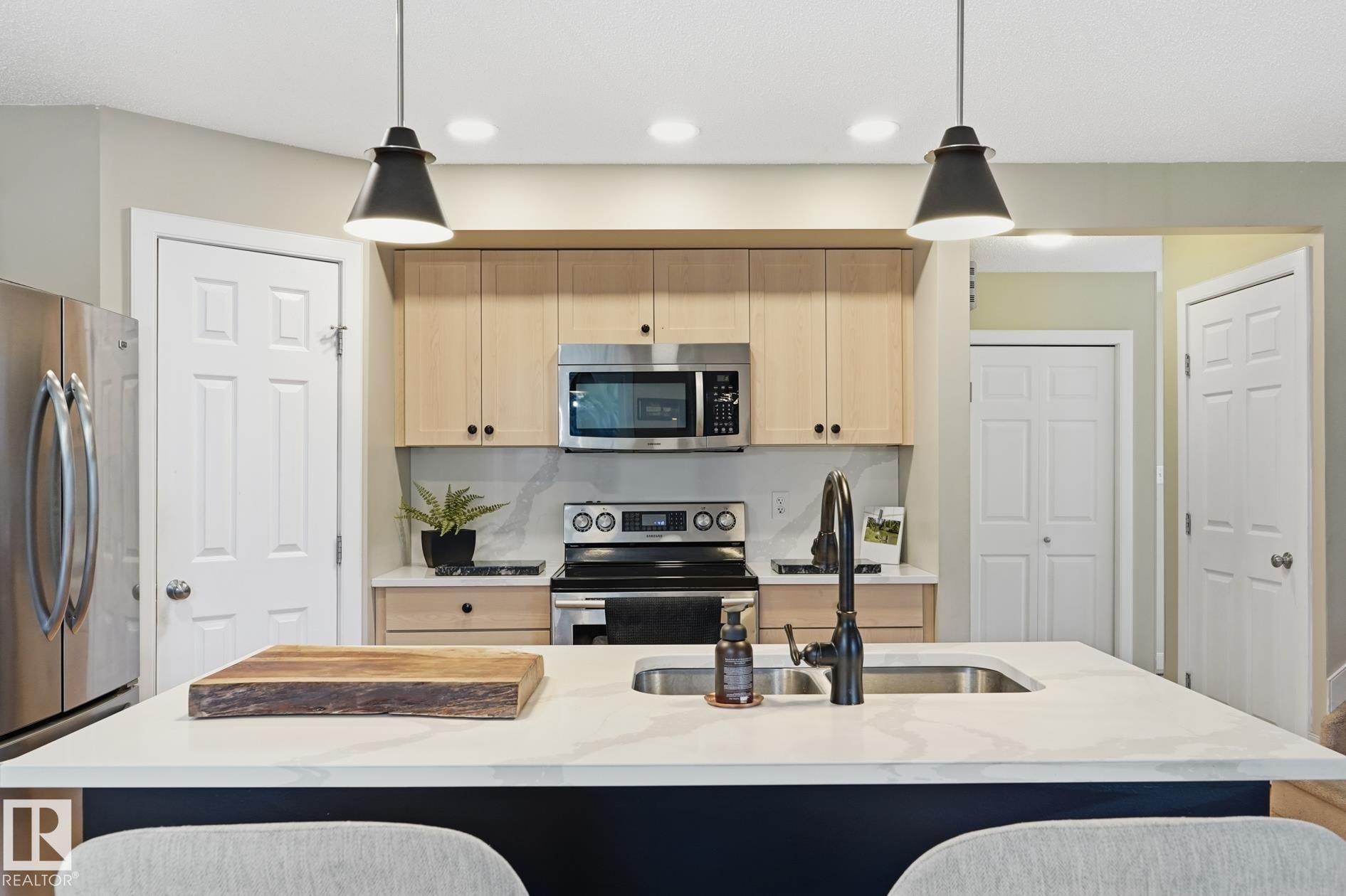 Kitchen featuring a center island with integrated sink, stainless steel appliances, light wood-finish cabinetry, and recessed lighting - 20007 131 Avenue Nw, Edmonton, AB
