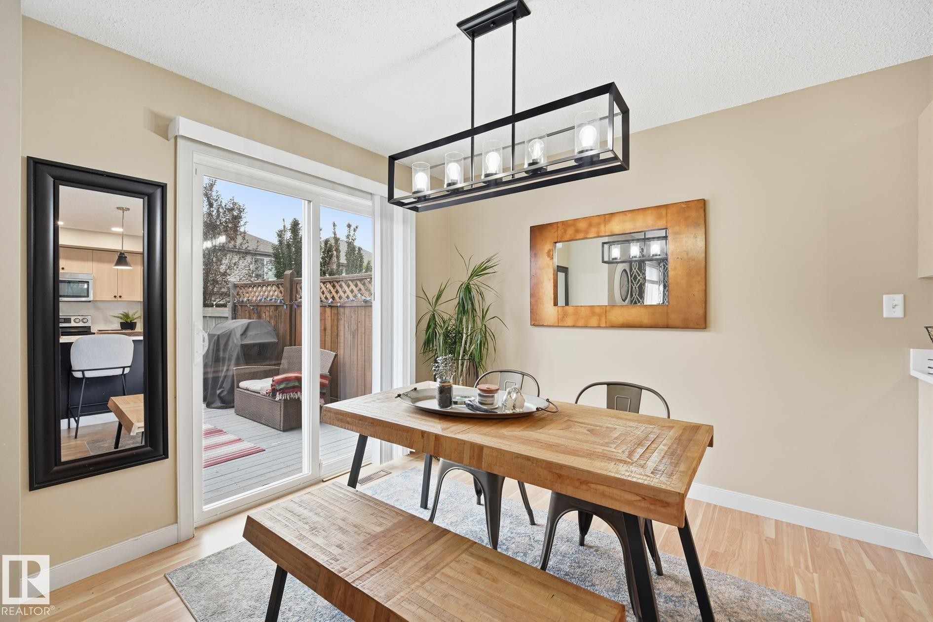 Dining area featuring wood-finish flooring, a rectangular linear chandelier, and a sliding glass door opening to an outdoor deck - 20007 131 Avenue Nw, Edmonton, AB