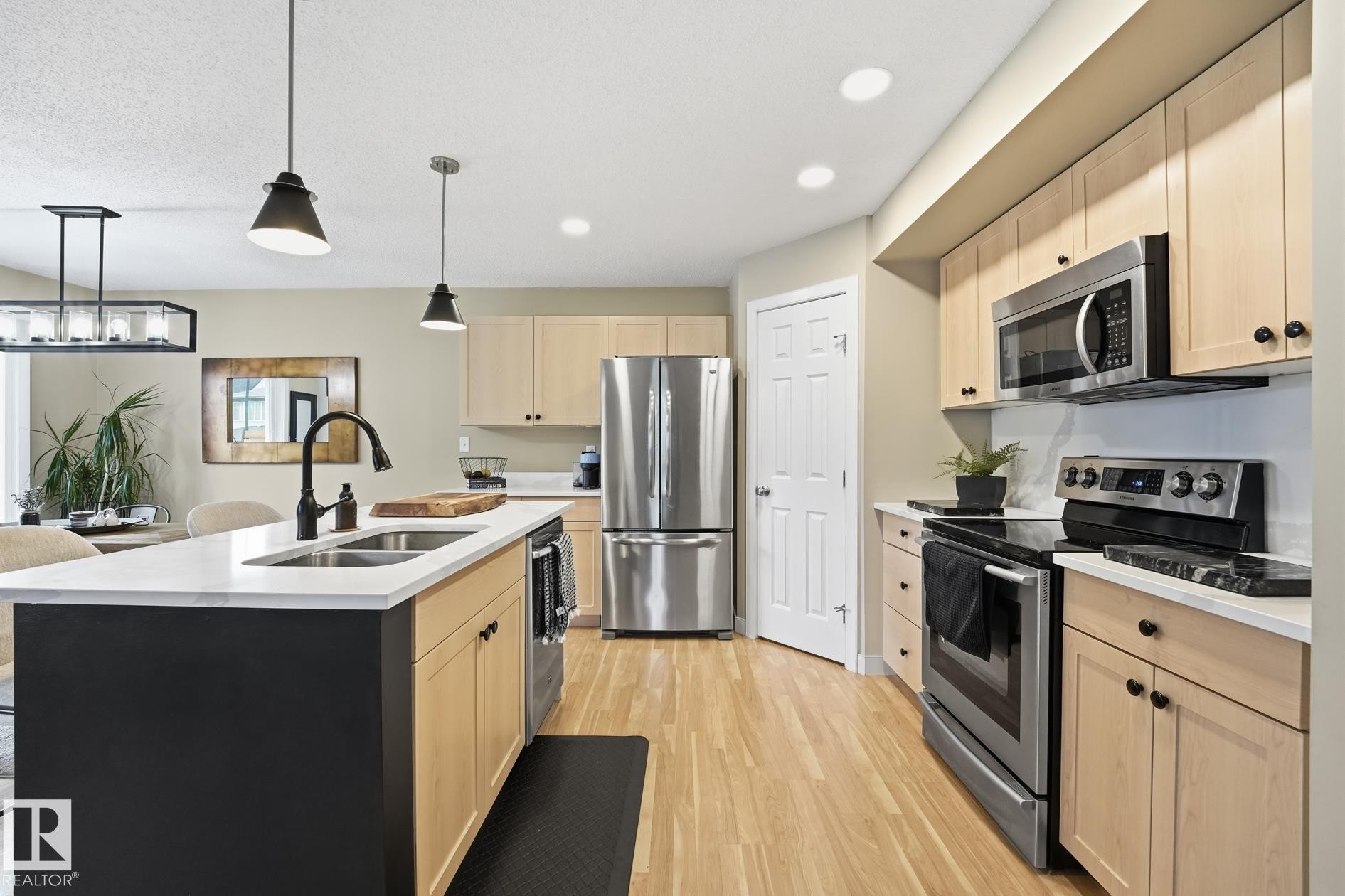 Kitchen featuring a center island with double basin sink, stainless steel appliances, light wood-finish cabinetry, and wood-finish flooring - 20007 131 Avenue Nw, Edmonton, AB