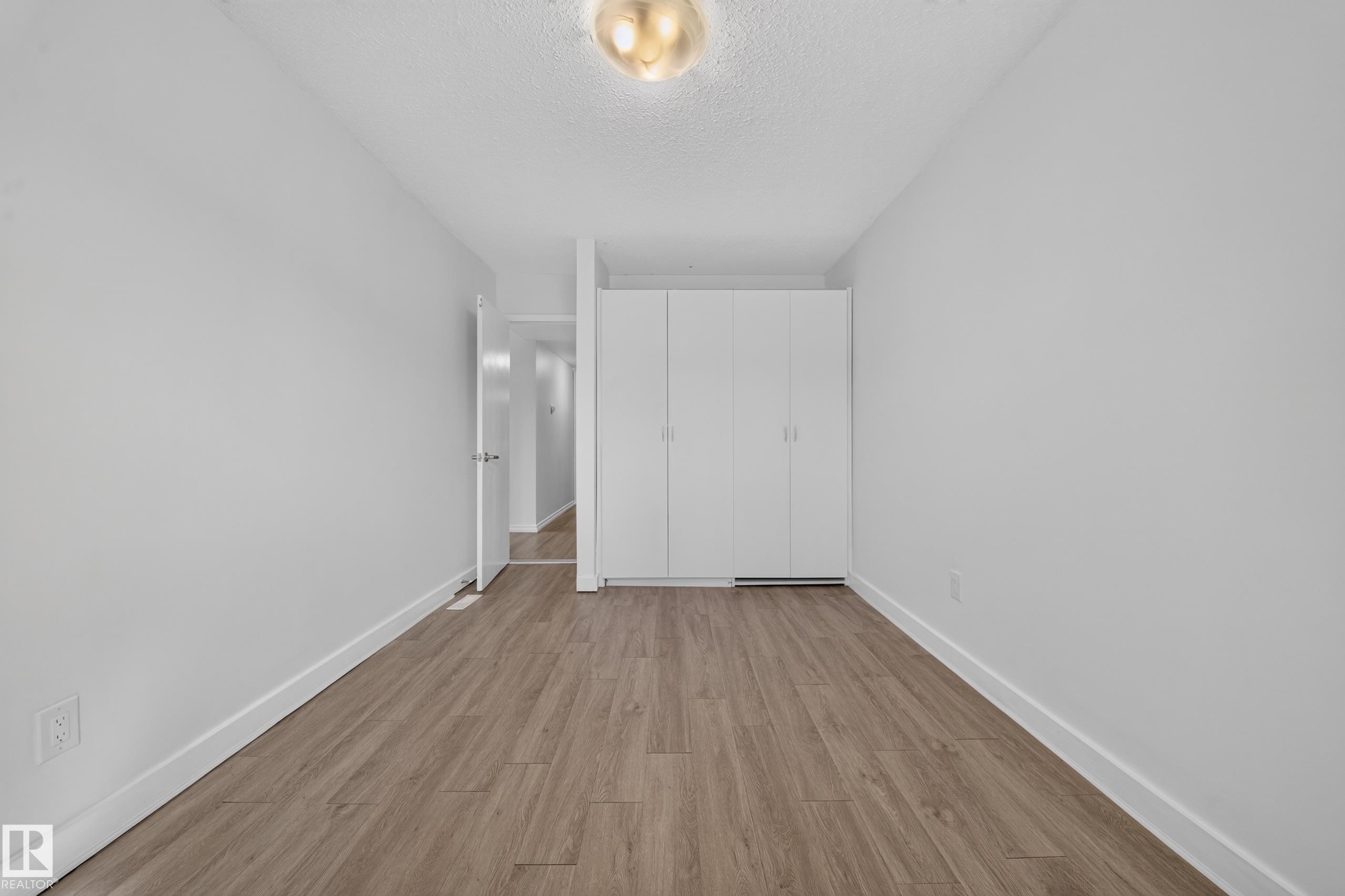 Spacious bedroom featuring warm wood-finish flooring, white painted walls, and a full-height built-in wardrobe system with clean-lined doors - 155 Marlborough Place Nw, Edmonton, AB