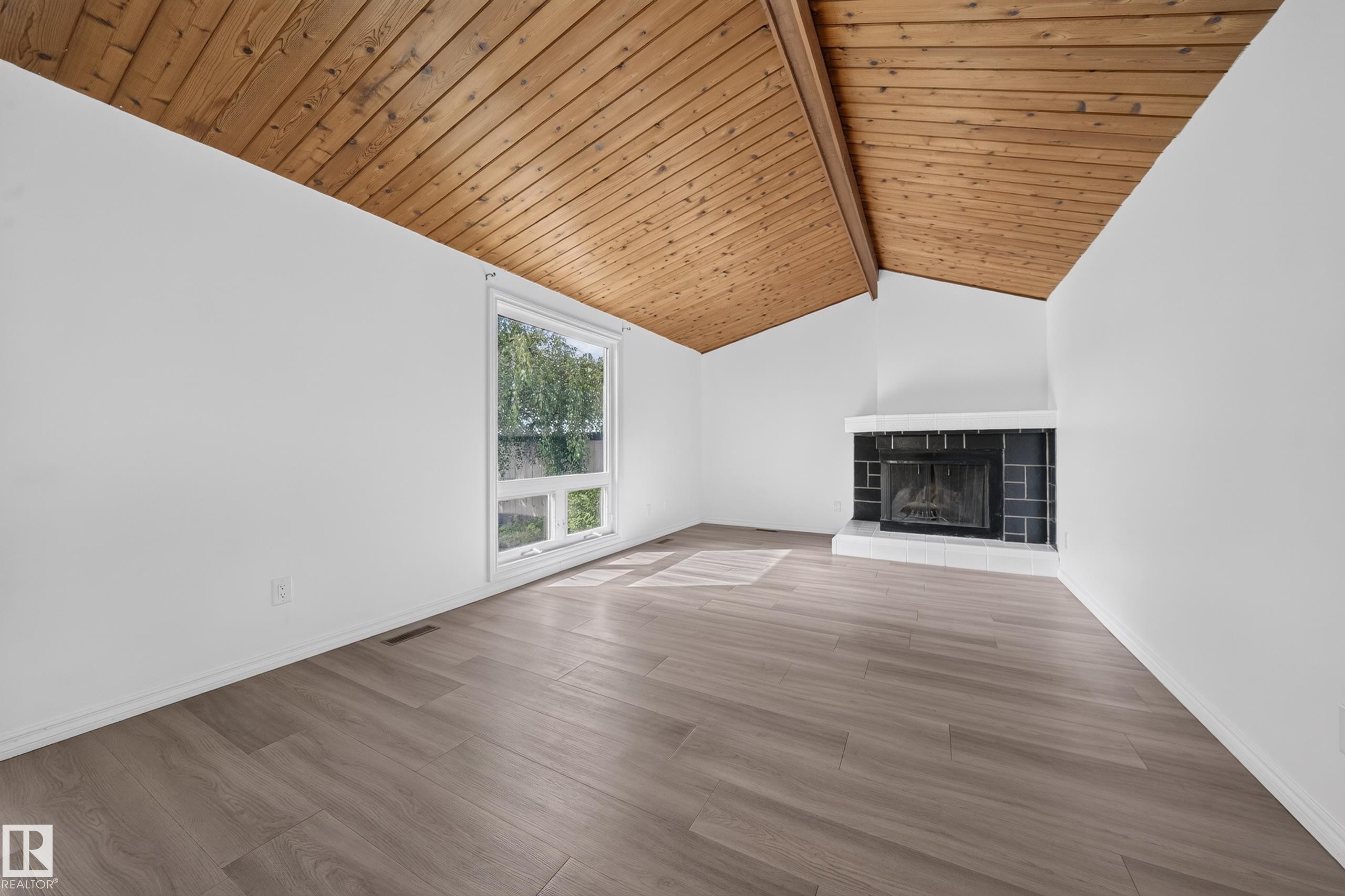 Vaulted wood-paneled ceiling, wood-finish flooring, corner fireplace with a tiled surround, and expansive window - 155 Marlborough Place Nw, Edmonton, AB