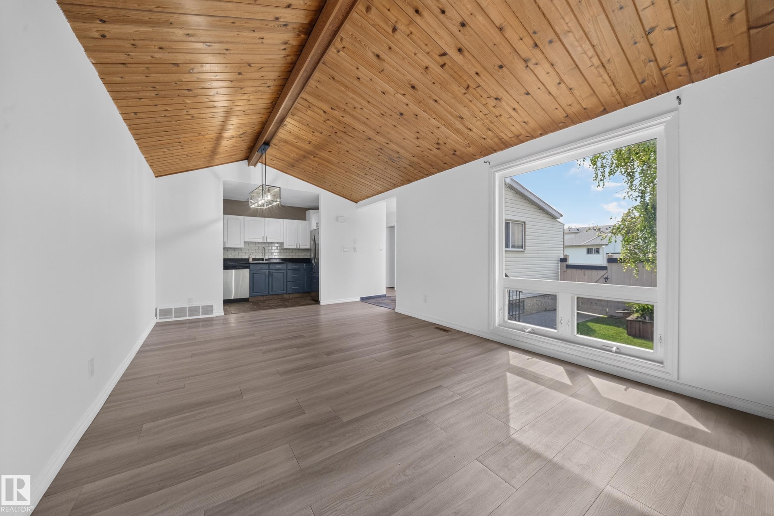 Vaulted wood-paneled ceiling with exposed beam, expansive window, wood-finish flooring, two-tone kitchen cabinetry, and stainless steel dishwasher - 155 Marlborough Place Nw, Edmonton, AB