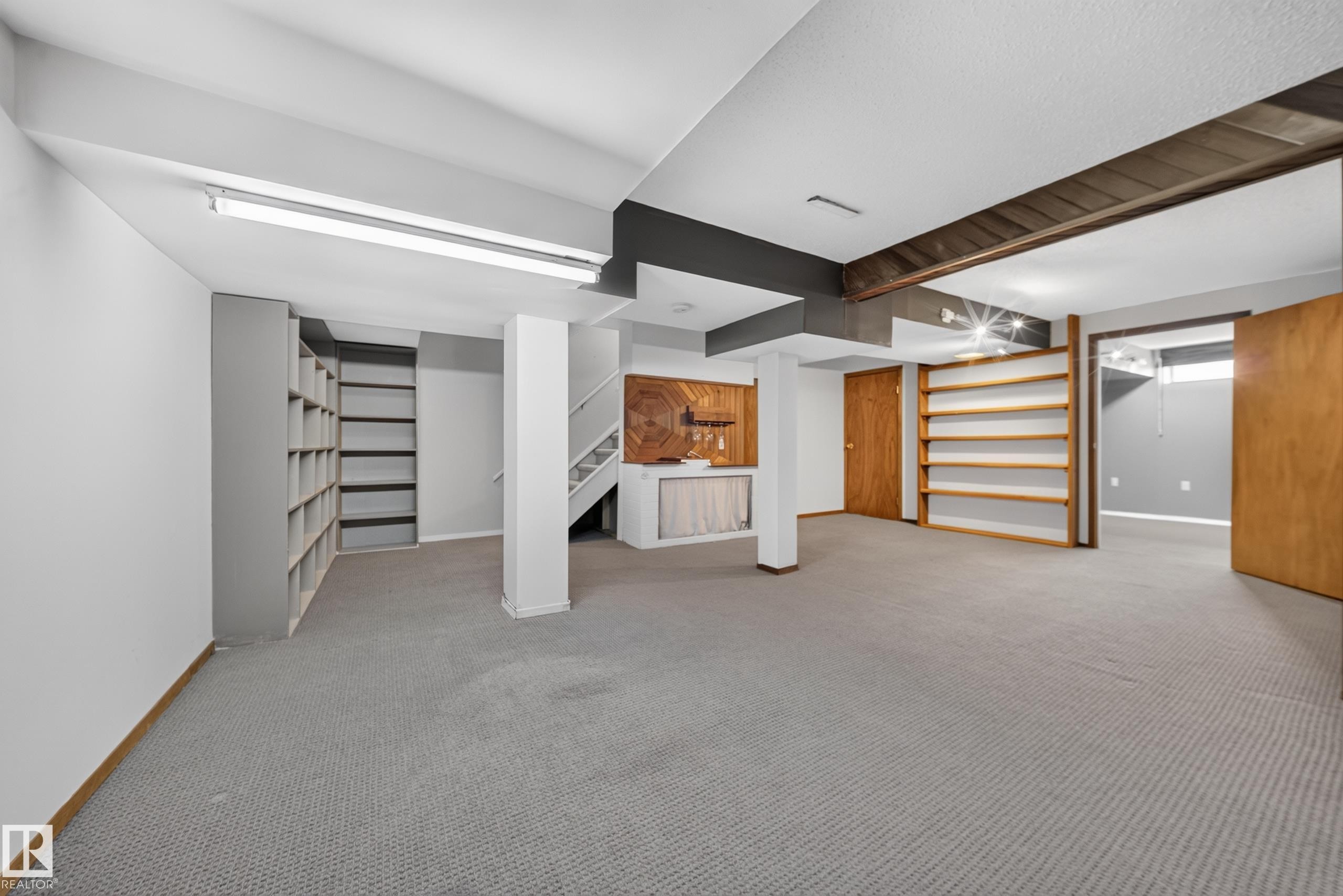 Spacious room with gray carpeting, extensive built-in shelving, wood-paneled accents, and exposed ceiling beams - 155 Marlborough Place Nw, Edmonton, AB
