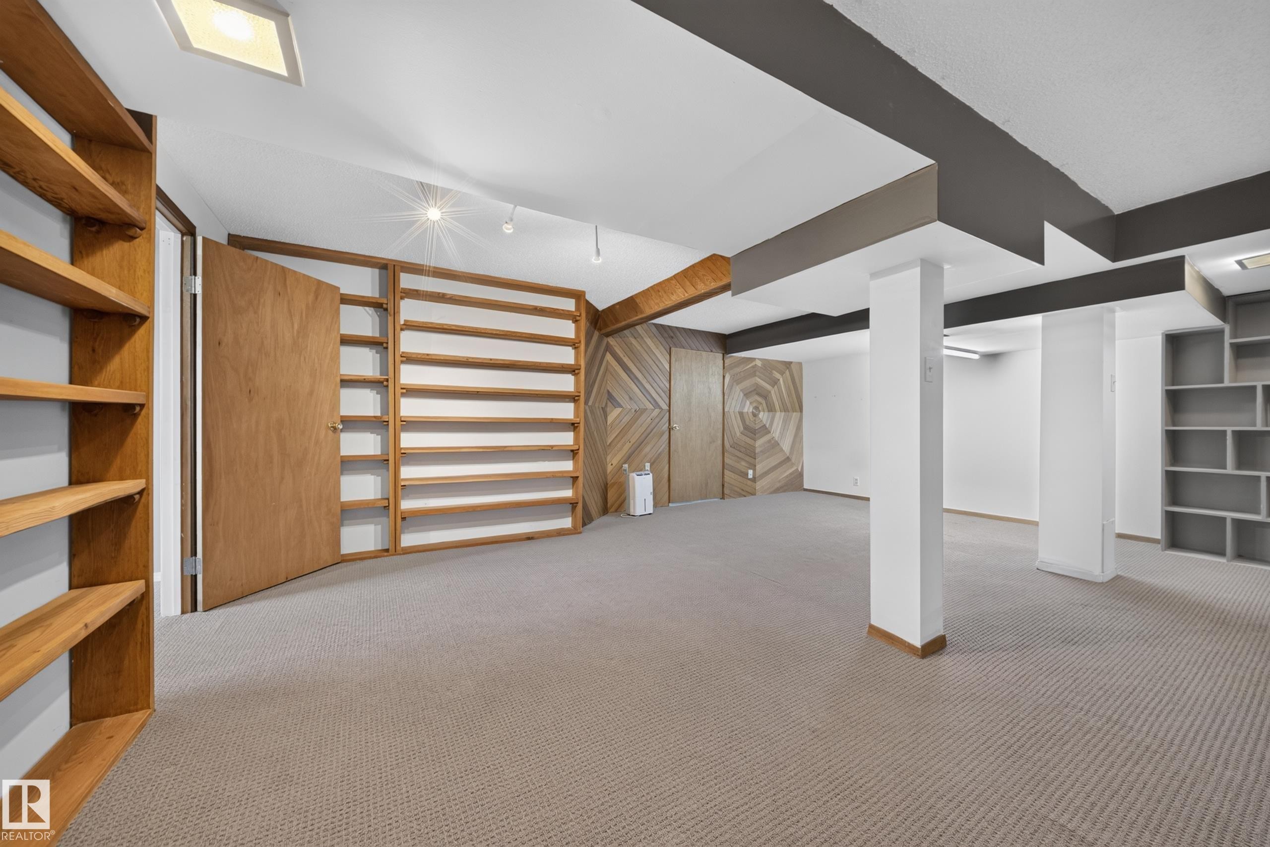 Expansive carpeted room featuring multiple built-in shelving units, wood-finish accent walls, and recessed lighting - 155 Marlborough Place Nw, Edmonton, AB