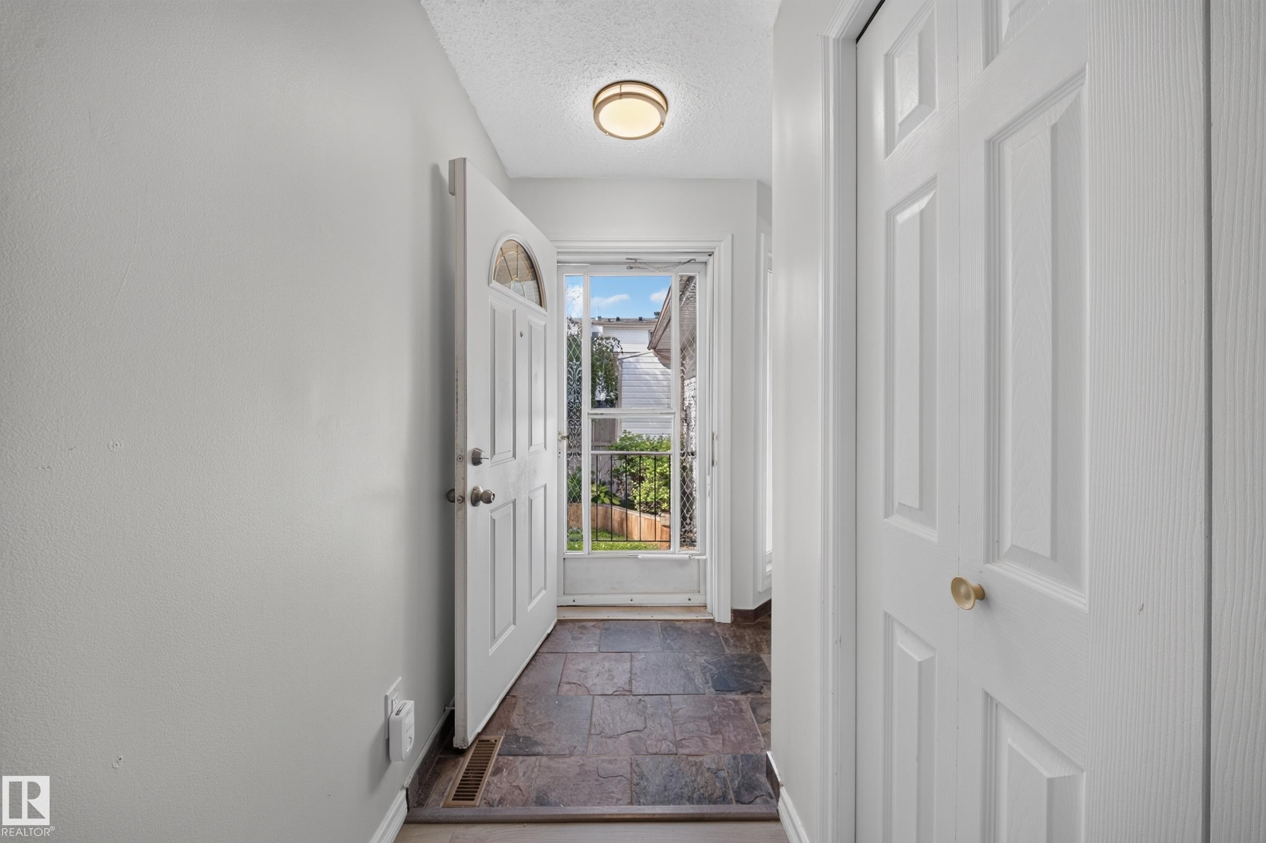 Foyer featuring slate tile flooring, a white paneled entry door with an arched glass insert, and a flush mount ceiling light - 155 Marlborough Place Nw, Edmonton, AB