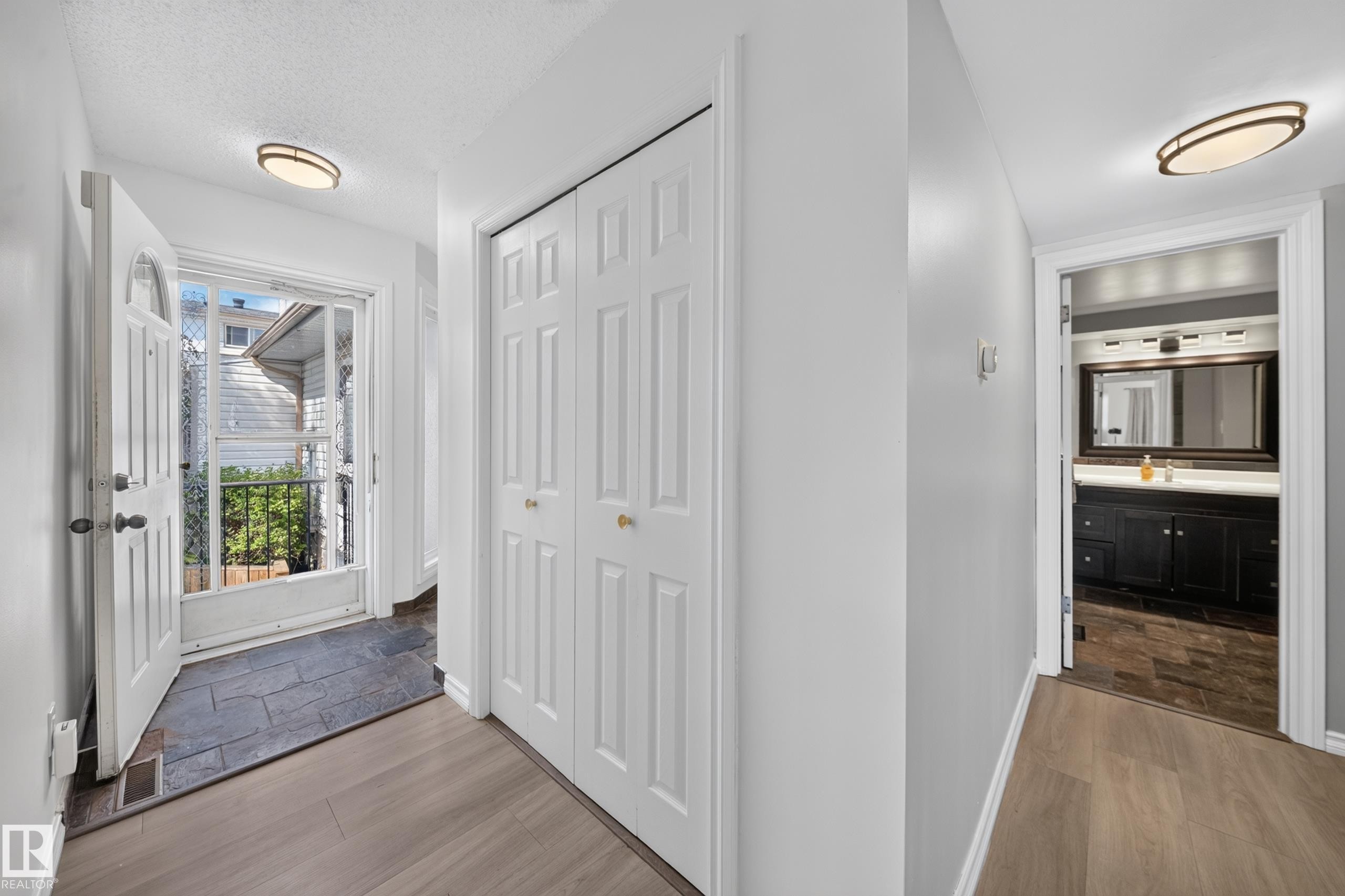 Entry foyer featuring slate-style tile flooring, wood-finish flooring, and white bi-fold closet doors - 155 Marlborough Place Nw, Edmonton, AB