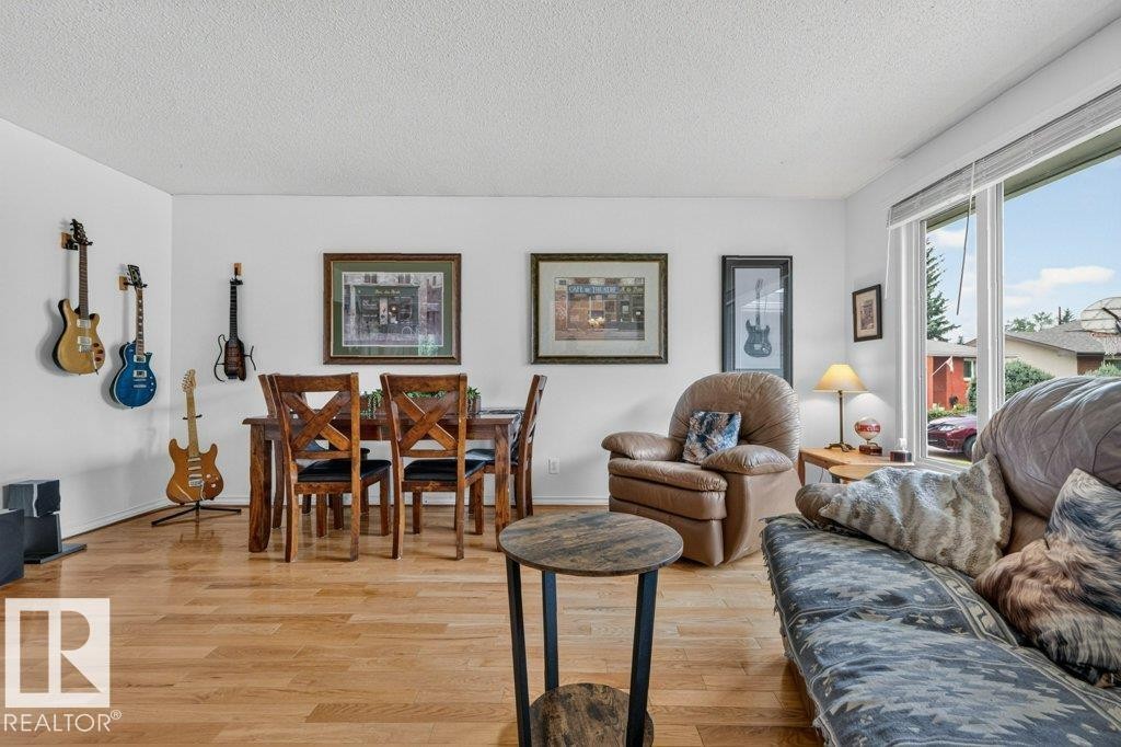 Open-concept living area featuring light wood-finish flooring, white walls, a large picture window, and a dedicated dining space with a dark wood table and chairs - 11131 35A Avenue Nw, Edmonton, AB - Indoor Photo Showing Living Room