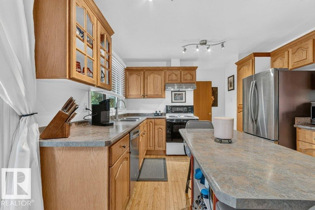 Kitchen featuring wood-finish cabinetry, stainless-steel appliances, and an elongated island with an overhang - 11131 35A Avenue Nw, Edmonton, AB - Indoor Photo Showing Kitchen With Double Sink