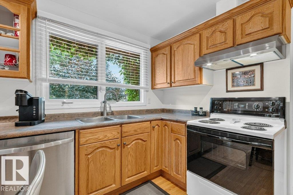 Kitchen featuring wood-finish cabinetry, a double basin stainless steel sink, and a white electric range with a stainless steel range hood - 11131 35A Avenue Nw, Edmonton, AB - Indoor Photo Showing Kitchen With Double Sink