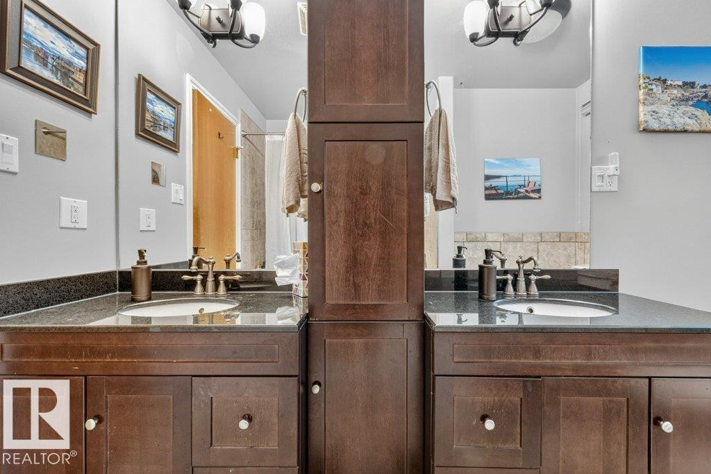 Dual vanity featuring dark wood cabinetry, integrated sinks, dark stone countertops, and individual mirrors - 11131 35A Avenue Nw, Edmonton, AB - Indoor Photo Showing Bathroom