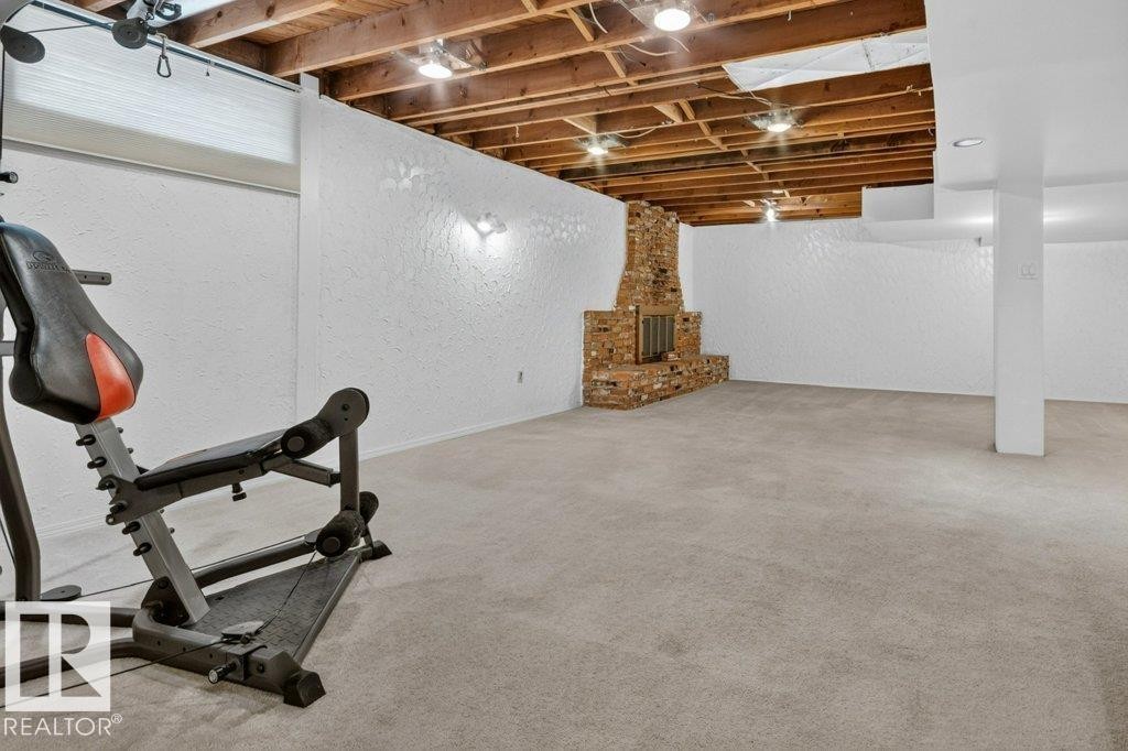 Spacious finished lower level featuring a brick fireplace, exposed wood ceiling beams, recessed lighting, and carpet flooring - 11131 35A Avenue Nw, Edmonton, AB - Indoor Photo Showing Basement