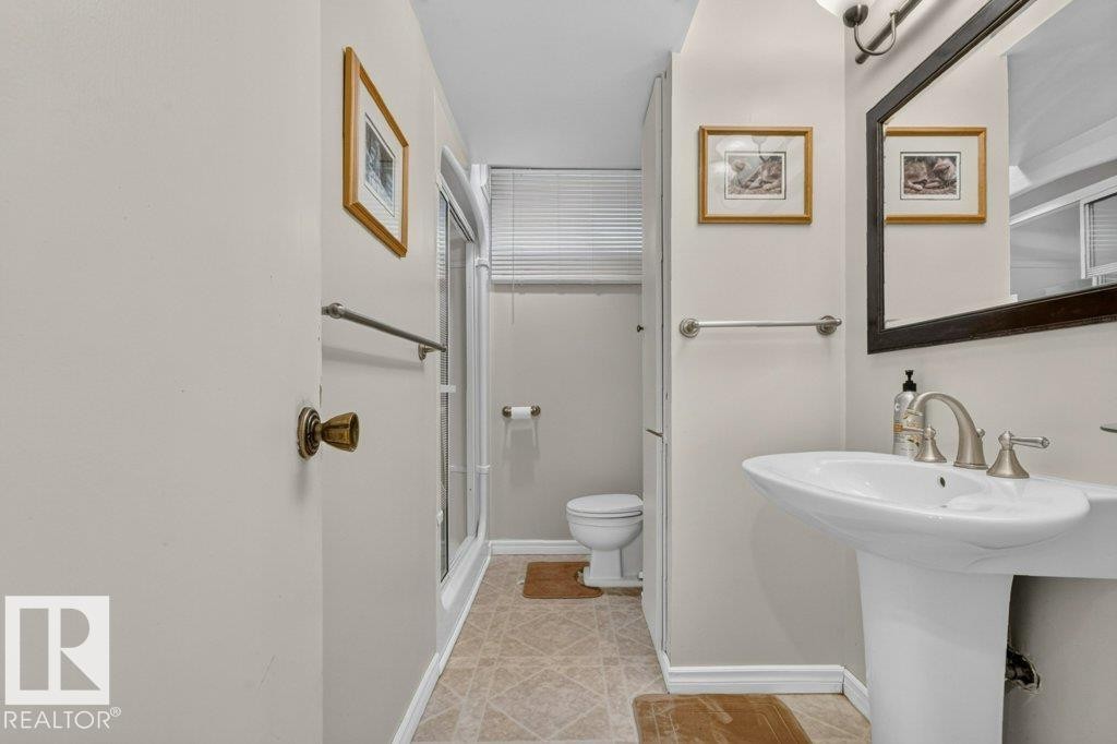 Bathroom featuring a pedestal sink, brushed nickel faucet, wall-mounted mirror with dark frame, shower enclosure with glass door, and a toilet - 11131 35A Avenue Nw, Edmonton, AB - Indoor Photo Showing Bathroom