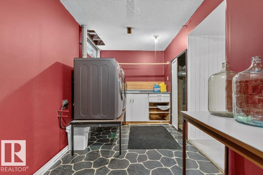 Dedicated laundry area featuring a patterned stone-look flooring, white base cabinetry with shelving, and a wood-finish countertop - 11131 35A Avenue Nw, Edmonton, AB - Indoor Photo Showing Other Room