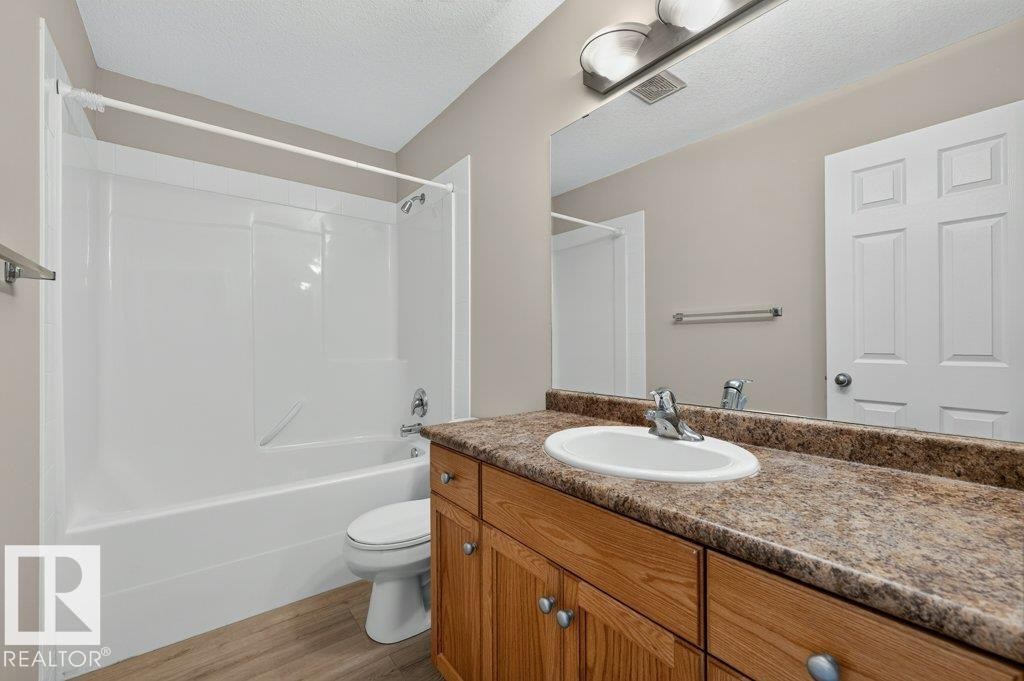 Bathroom featuring a white tub/shower combination, single vanity with a laminate countertop, wood-finish cabinetry, and a large wall mirror - #26 2816 34 Av Nw, Edmonton, AB