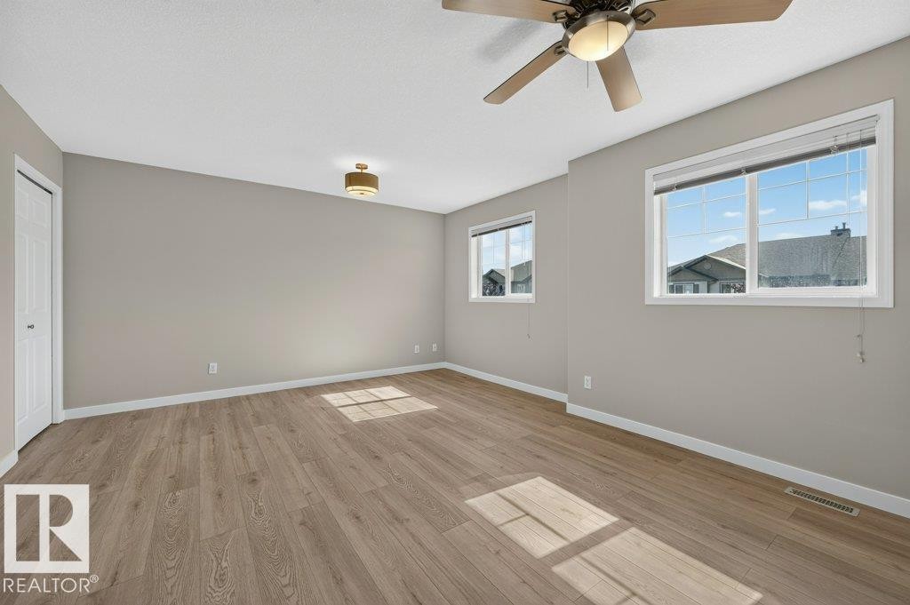 Wood-finish flooring, neutral wall paint, two large windows, a ceiling fan, and a flush-mount light fixture - #26 2816 34 Av Nw, Edmonton, AB