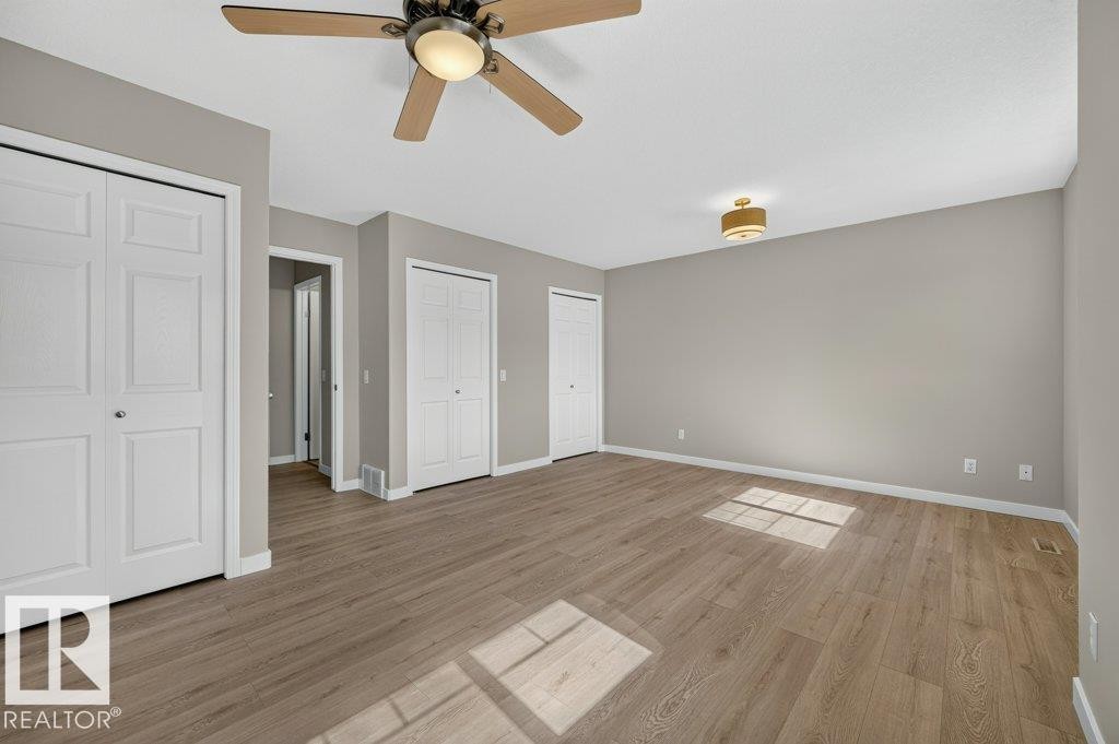 Wood-finish flooring, neutral wall tones, ceiling fan with integrated lighting, recessed ceiling light fixture, and multiple bi-fold closet doors - #26 2816 34 Av Nw, Edmonton, AB