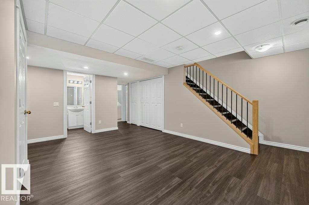 Wood-finish flooring, staircase with natural wood handrail and black metal spindles, recessed lighting, drop ceiling, and a bathroom vanity with a vessel sink - #26 2816 34 Av Nw, Edmonton, AB