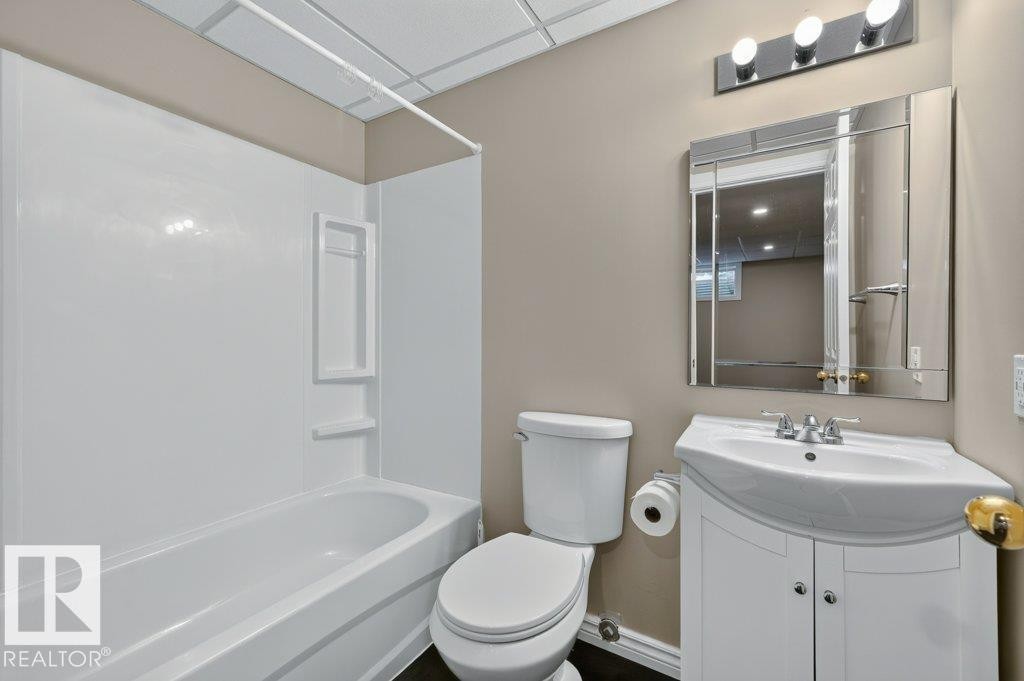 White built-in tub and shower unit, white vanity with integrated sink, chrome faucet, wall-mounted mirror, and vanity light fixture - #26 2816 34 Av Nw, Edmonton, AB