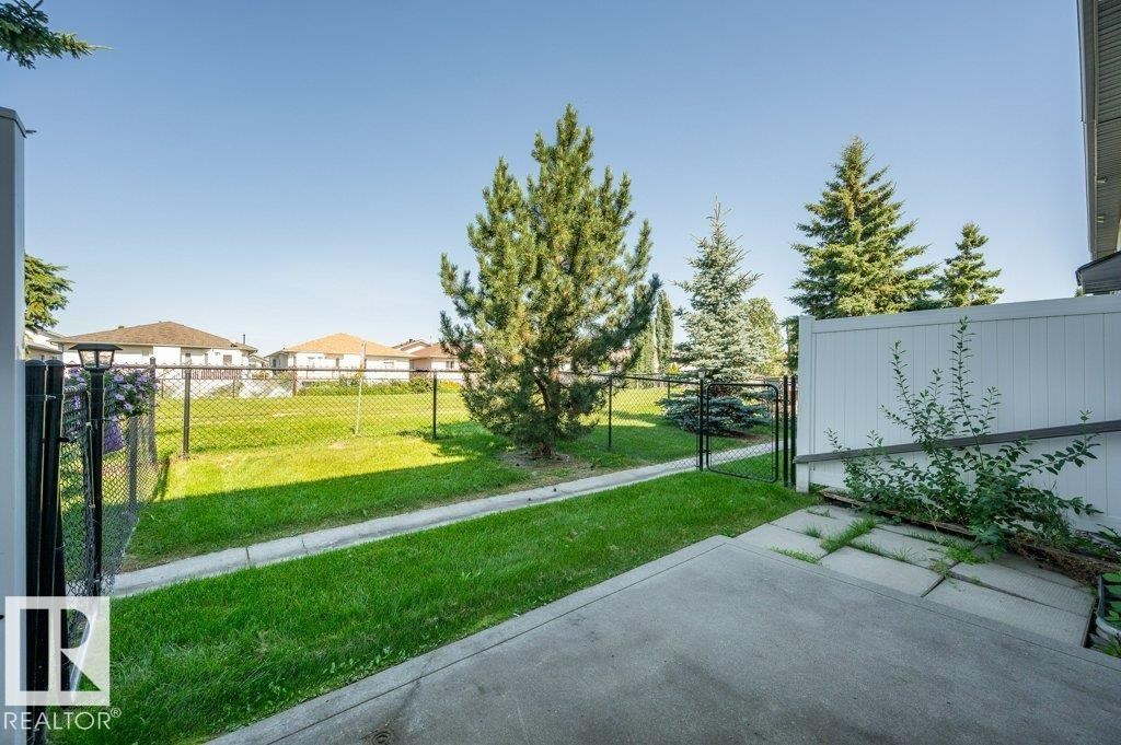 Expansive green space featuring mature trees, a chain-link fence, and a concrete patio - #26 2816 34 Av Nw, Edmonton, AB