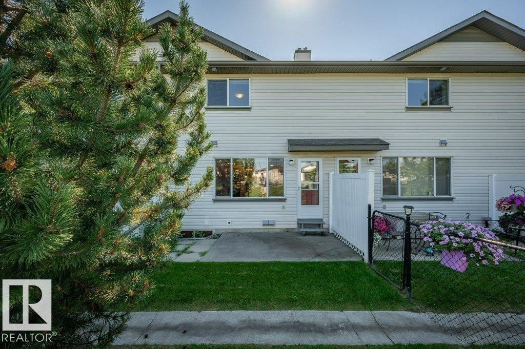 Rear exterior featuring white siding, a concrete patio, and a grass lawn - #26 2816 34 Av Nw, Edmonton, AB