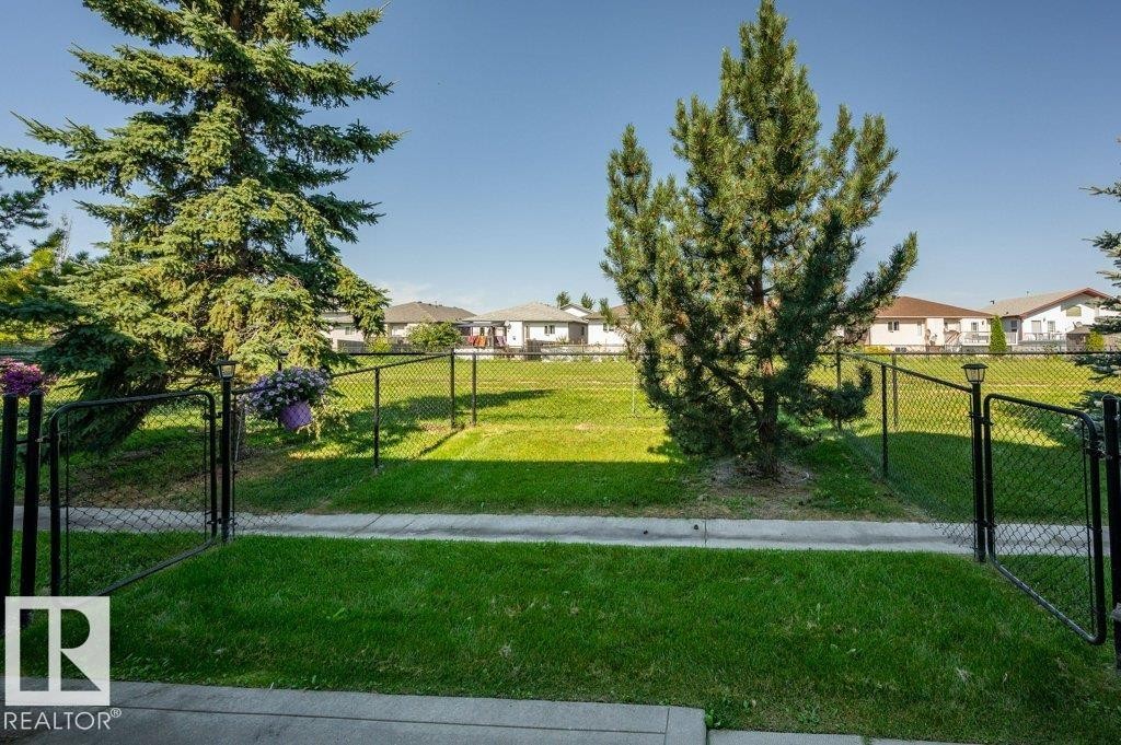 Expansive grassy area with mature evergreen trees and chain-link fencing - #26 2816 34 Av Nw, Edmonton, AB
