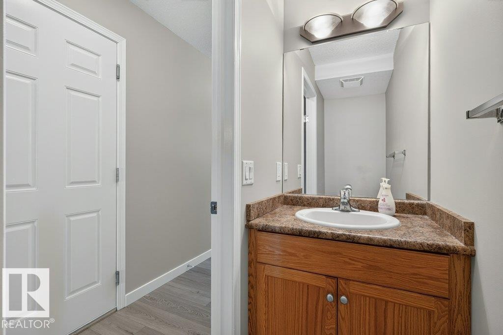 Wood-finish vanity with an integrated basin, a patterned countertop, and an overhead vanity light fixture - #26 2816 34 Av Nw, Edmonton, AB