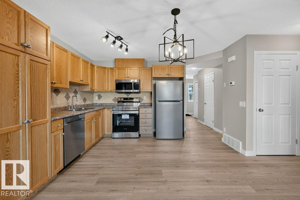 Kitchen featuring wood-finish cabinetry, stainless steel appliances, and a tile backsplash - #26 2816 34 Av Nw, Edmonton, AB