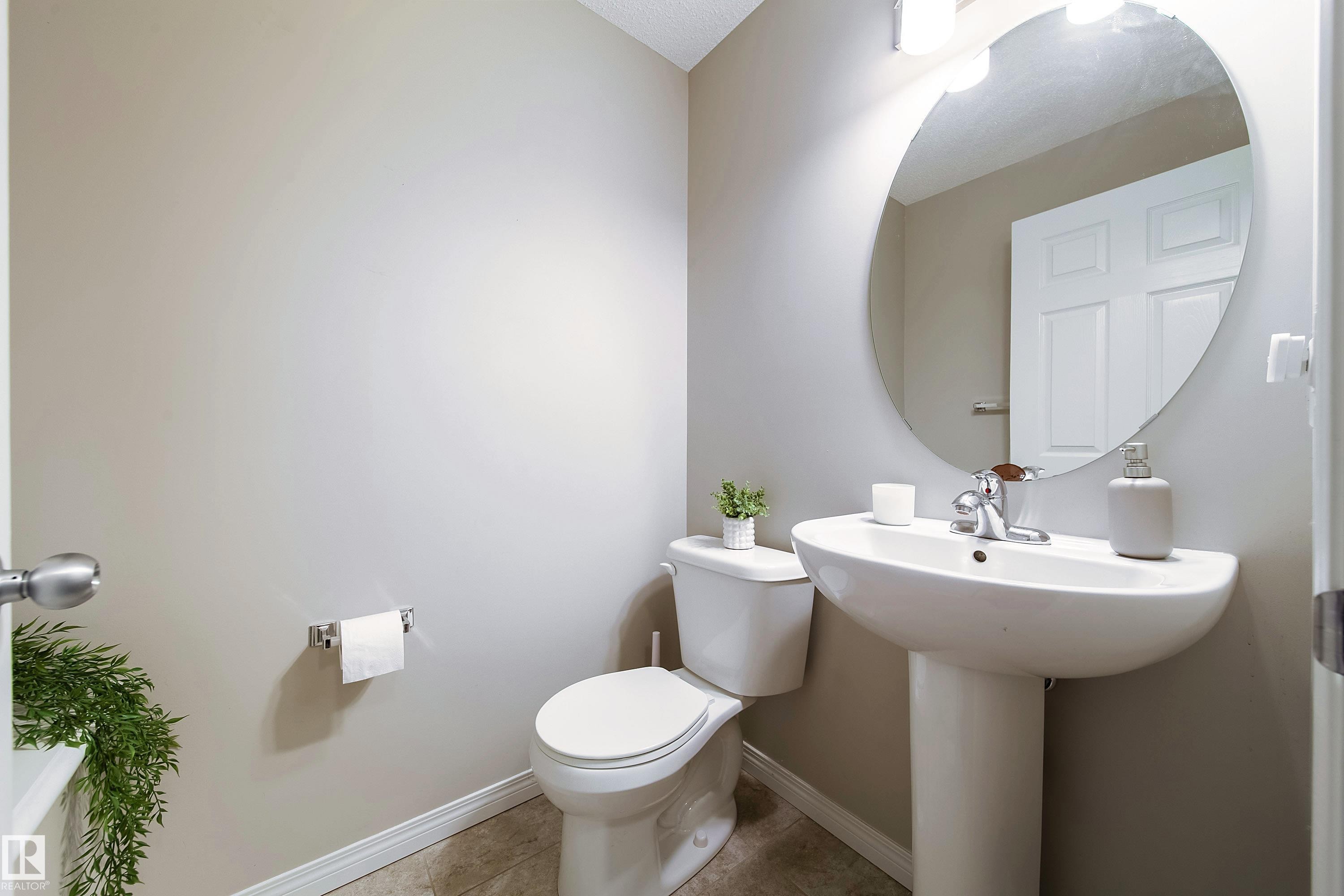Pedestal sink with chrome faucet, circular mirror, and wall-mounted light fixture - 3211 Cherry Crescent Sw, Edmonton, AB