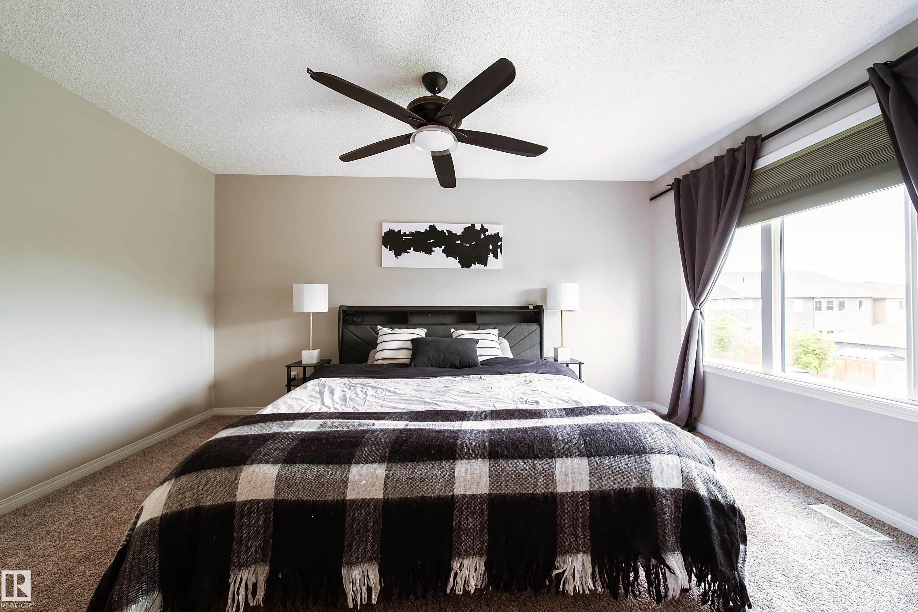 Neutral-toned walls, ceiling fan with integrated lighting, expansive window with roller shade, and textured carpeting - 3211 Cherry Crescent Sw, Edmonton, AB