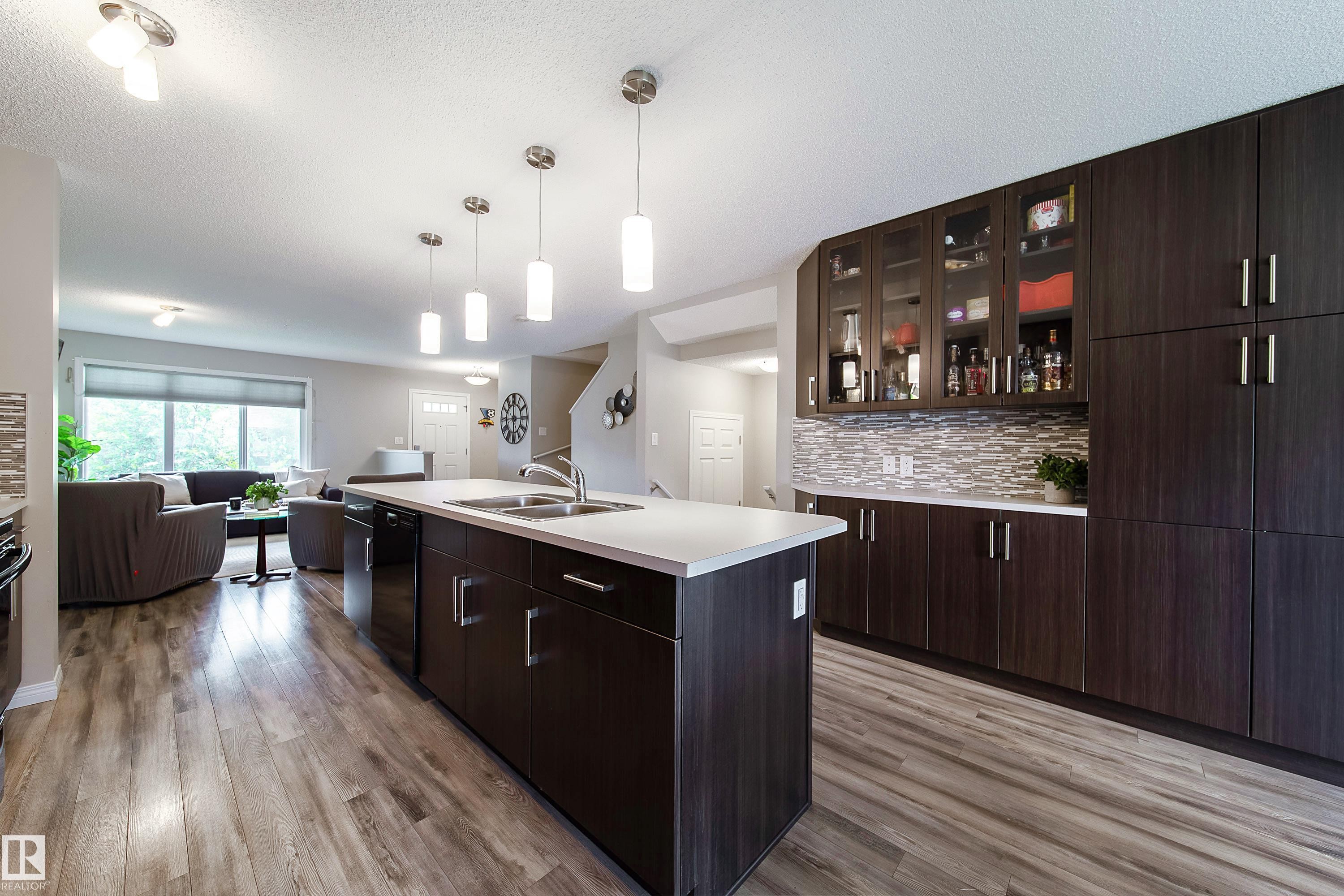 Kitchen featuring a central island with a double sink, dark wood-finish cabinetry, and a textured tile backsplash - 3211 Cherry Crescent Sw, Edmonton, AB