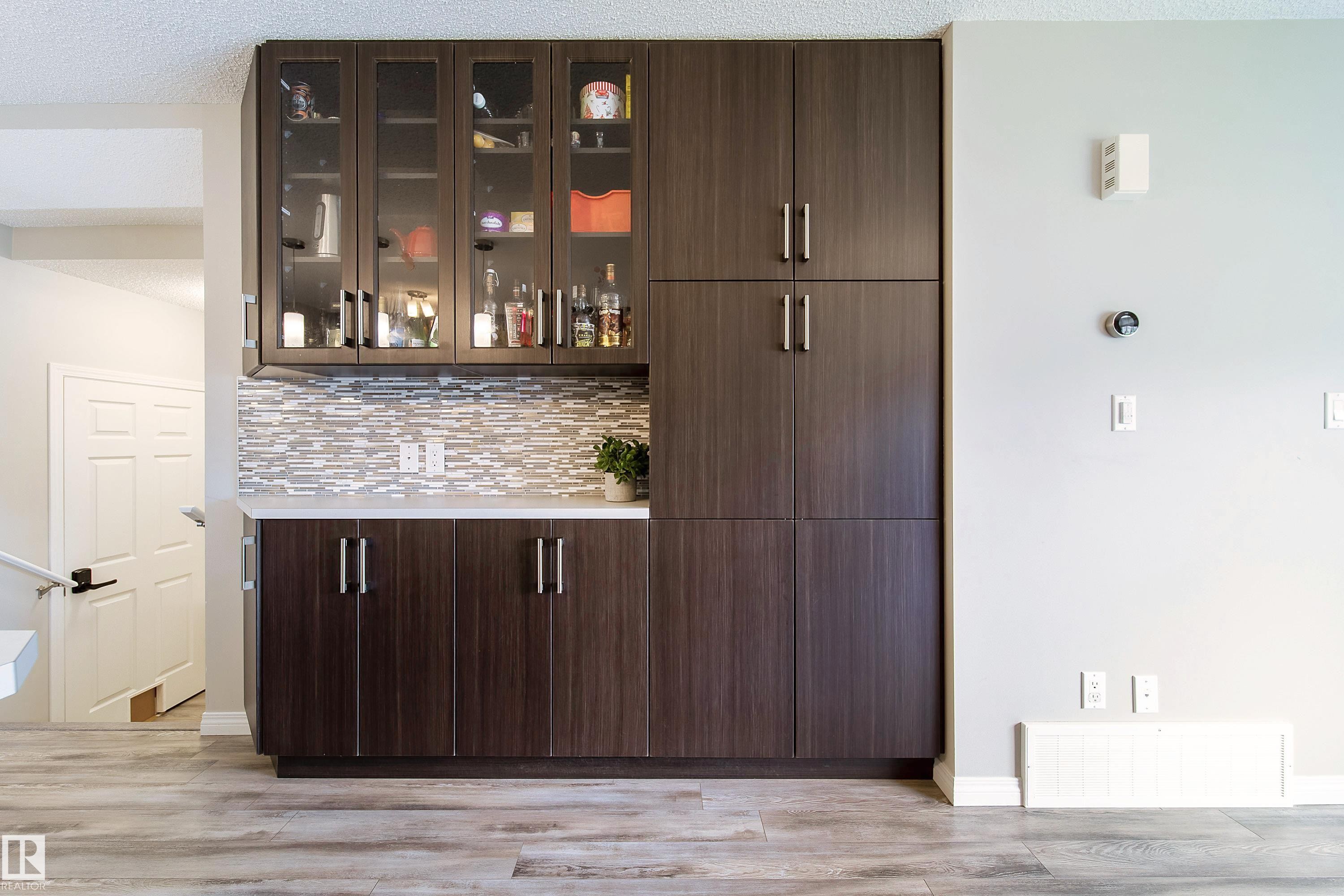 Built-in cabinetry with glass-front uppers and solid lower doors, subway tile backsplash, light-toned countertop, and wood-finish flooring - 3211 Cherry Crescent Sw, Edmonton, AB