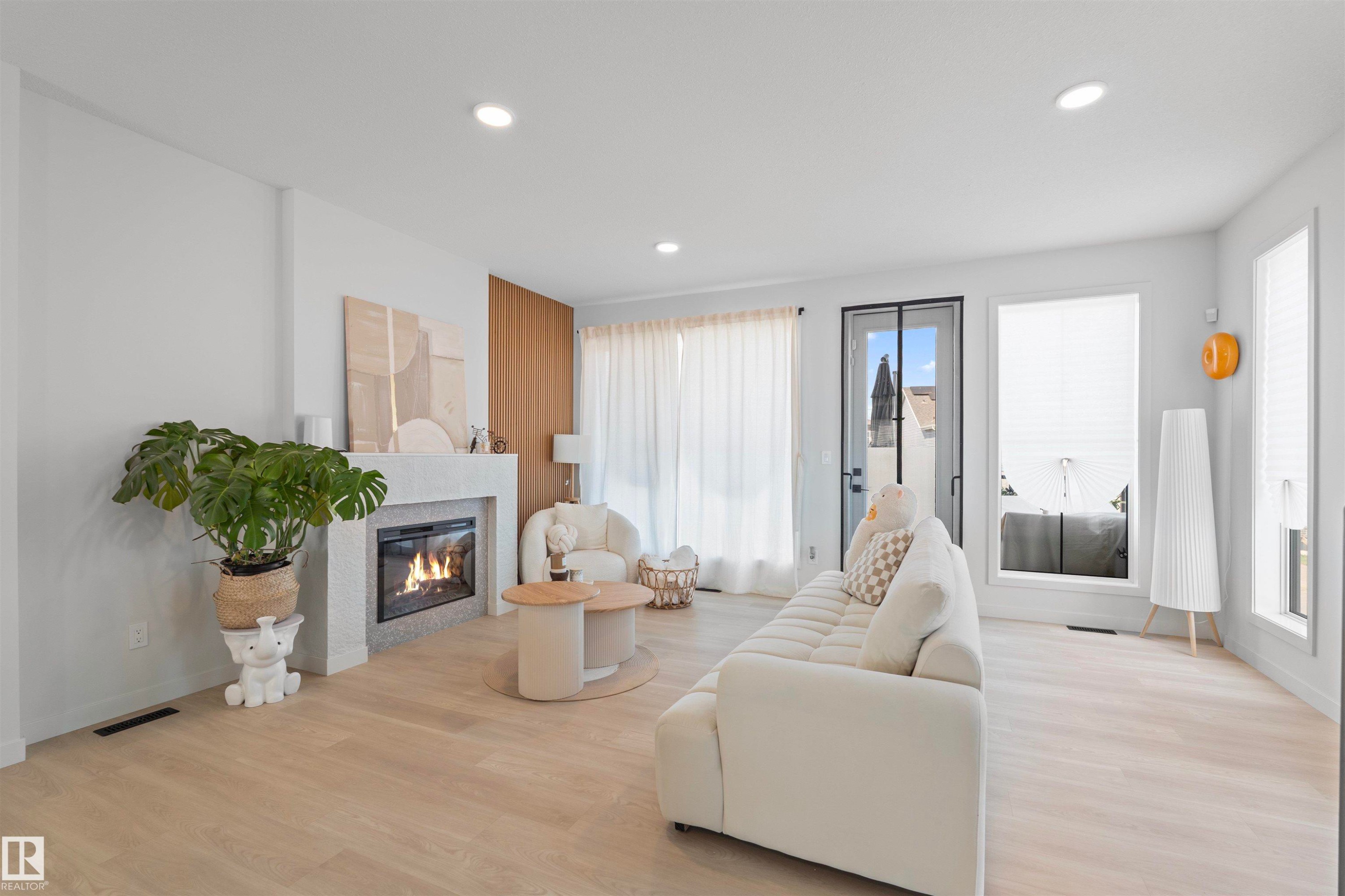 Recessed lighting illuminates wood-finish flooring and a fireplace with a textured surround - 8047 227 Street Nw, Edmonton, AB