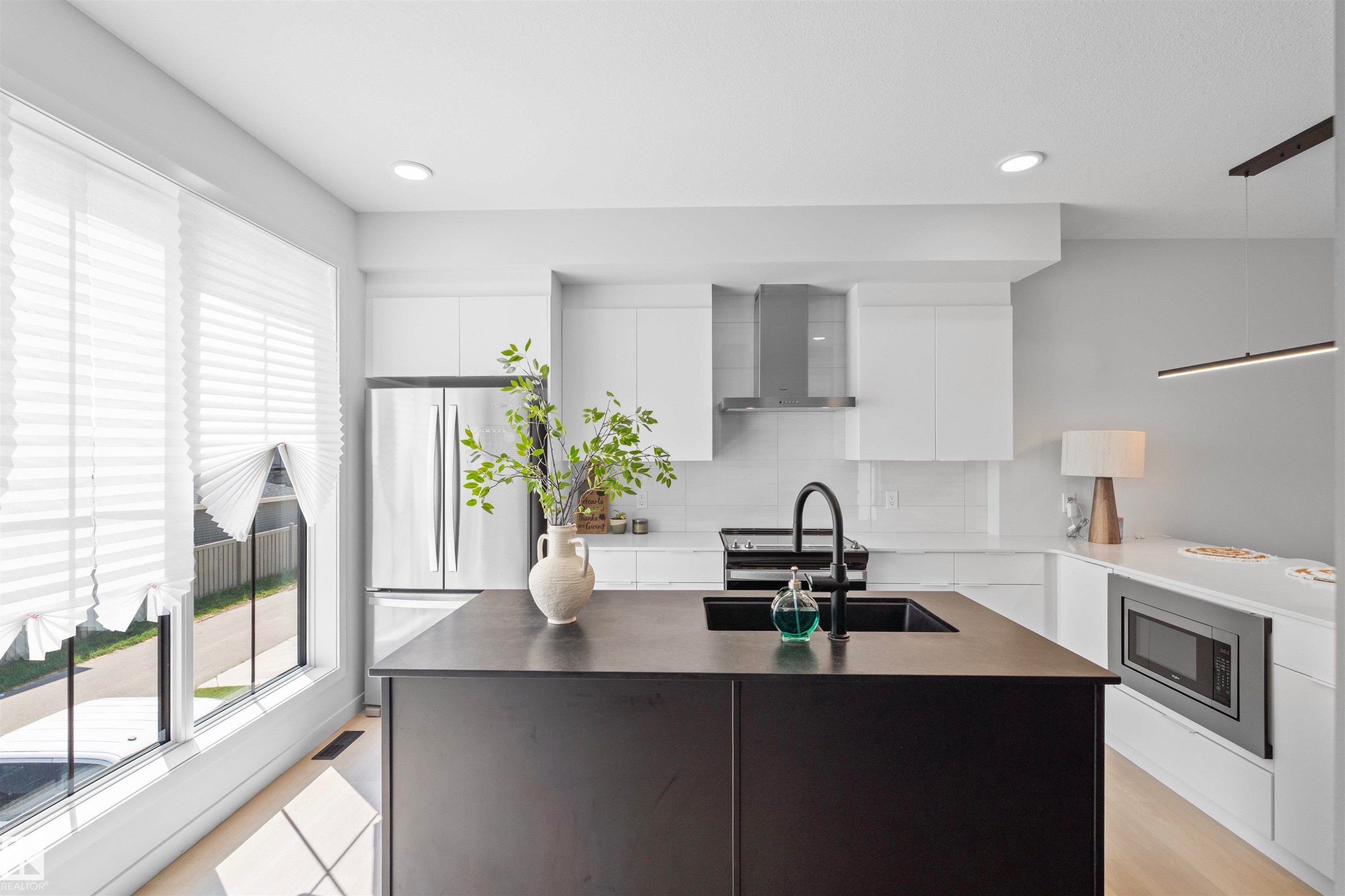 Contemporary kitchen featuring a black central island, integrated sink, and stainless steel appliances - 8047 227 Street Nw, Edmonton, AB