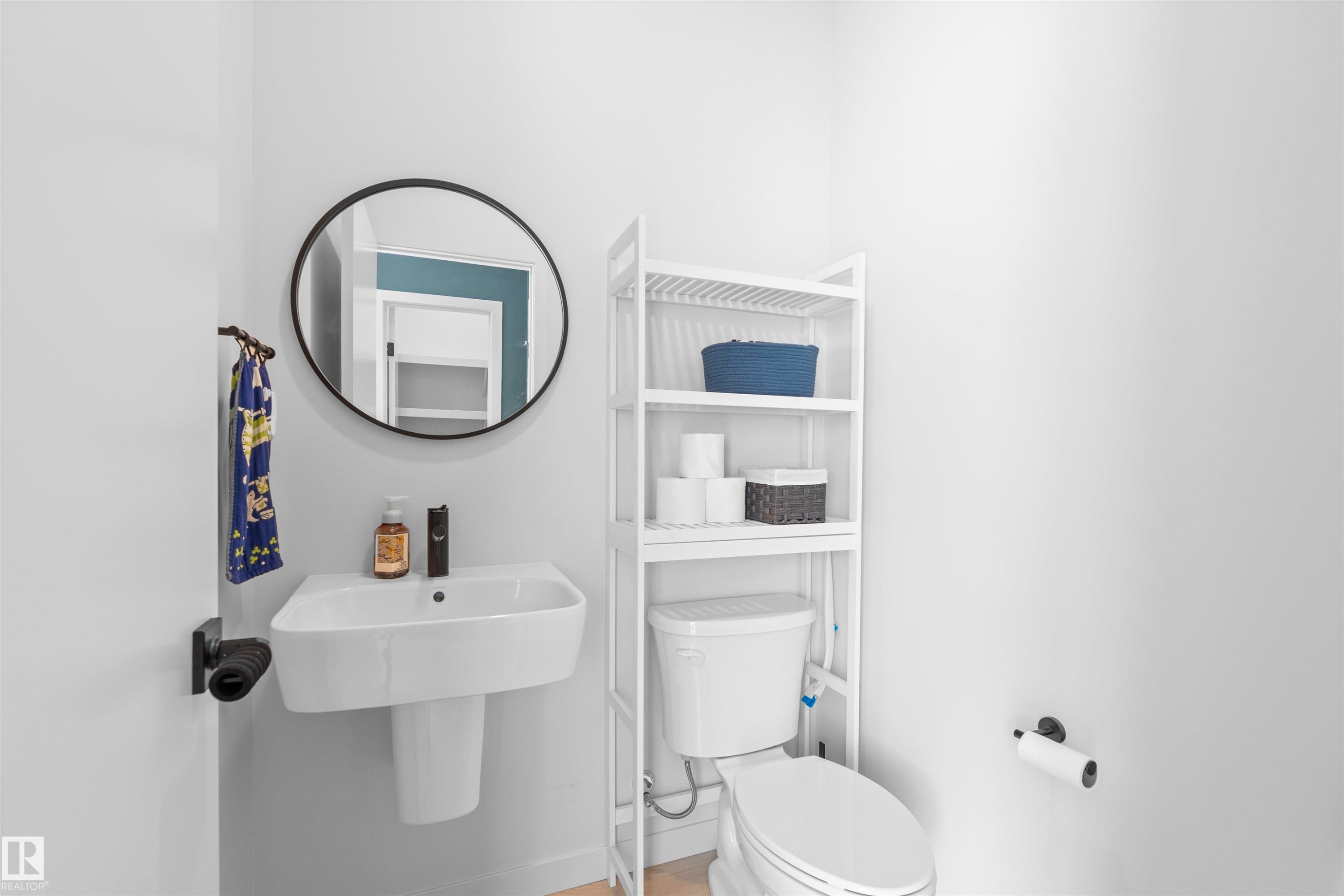 Pedestal sink with dark-toned fixtures, a round mirror, and a white toilet - 8047 227 Street Nw, Edmonton, AB
